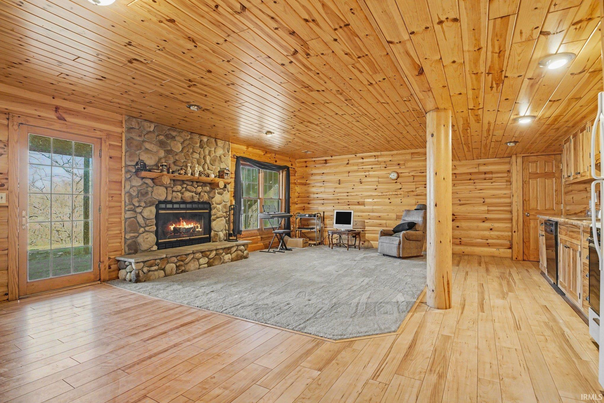 Unfurnished living room with a fireplace, wooden ceiling, light wood finished floors, and log walls