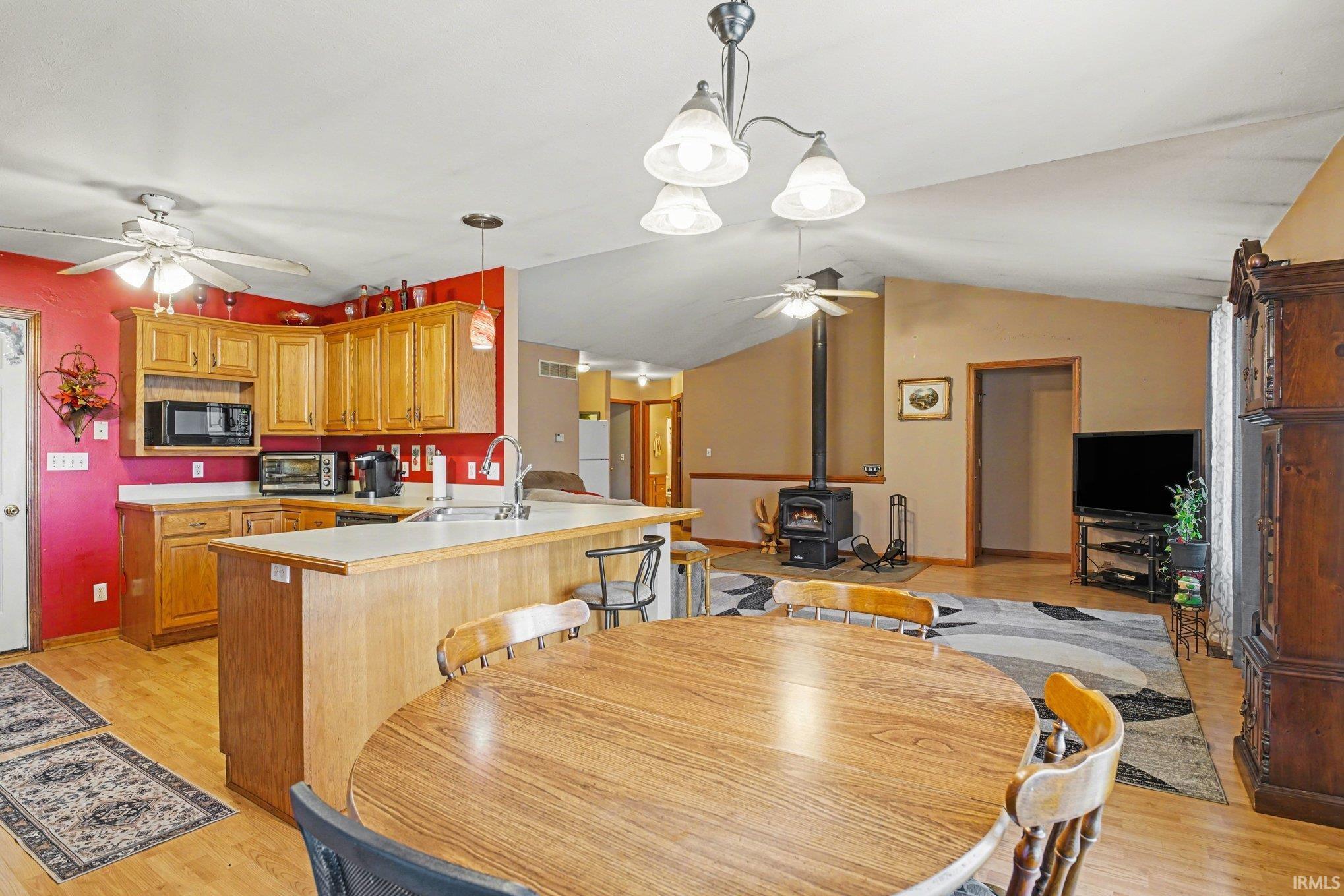 Dining area with a ceiling fan, a wood stove, light wood-style floors, and vaulted ceiling