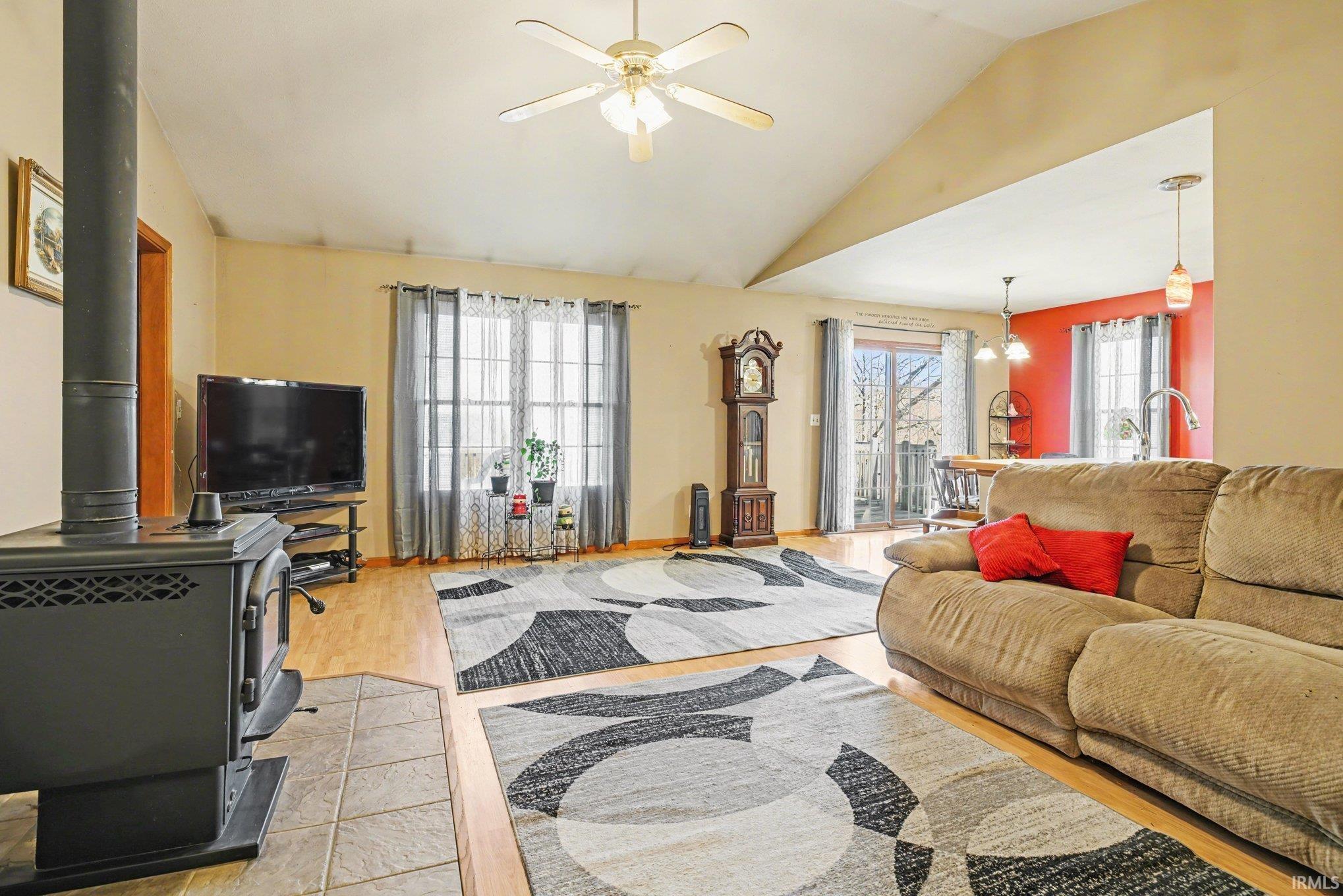 Living area featuring a wood stove, a ceiling fan, lofted ceiling, and light wood-style flooring