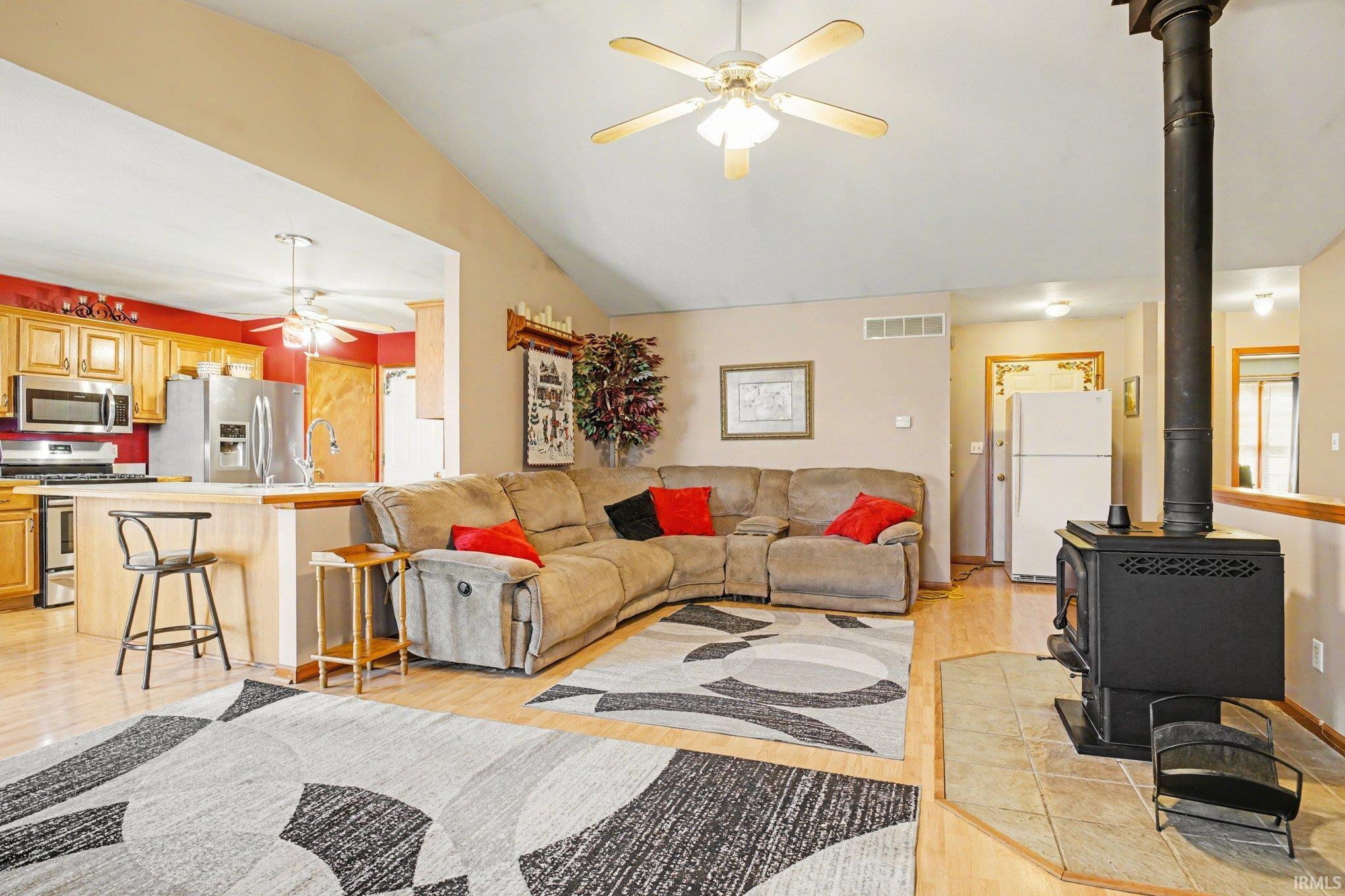 Living area featuring ceiling fan, vaulted ceiling, a wood stove, and light wood-type flooring