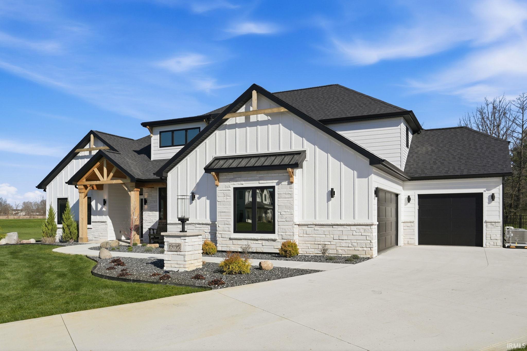 Modern farmhouse with an attached garage, roof with shingles, board and batten siding, and stone siding
