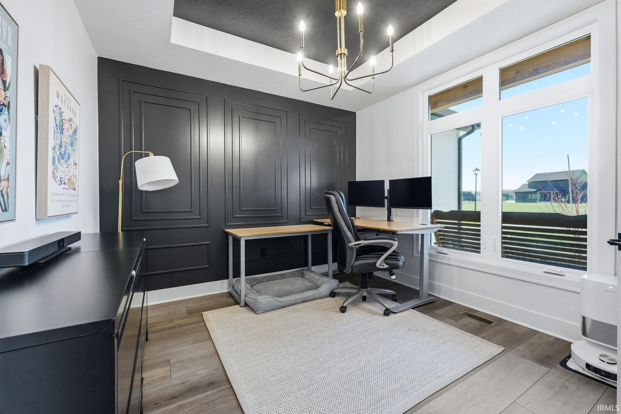 Office area featuring a raised ceiling, light wood-type flooring, a chandelier, and an accent wall