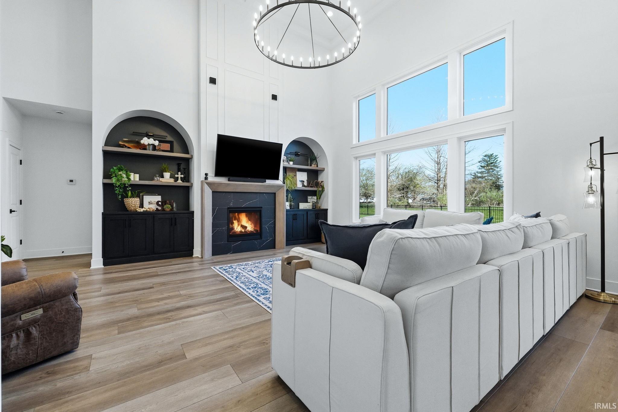 Living area with a high ceiling, built in shelves, a fireplace, light wood-type flooring, and a chandelier