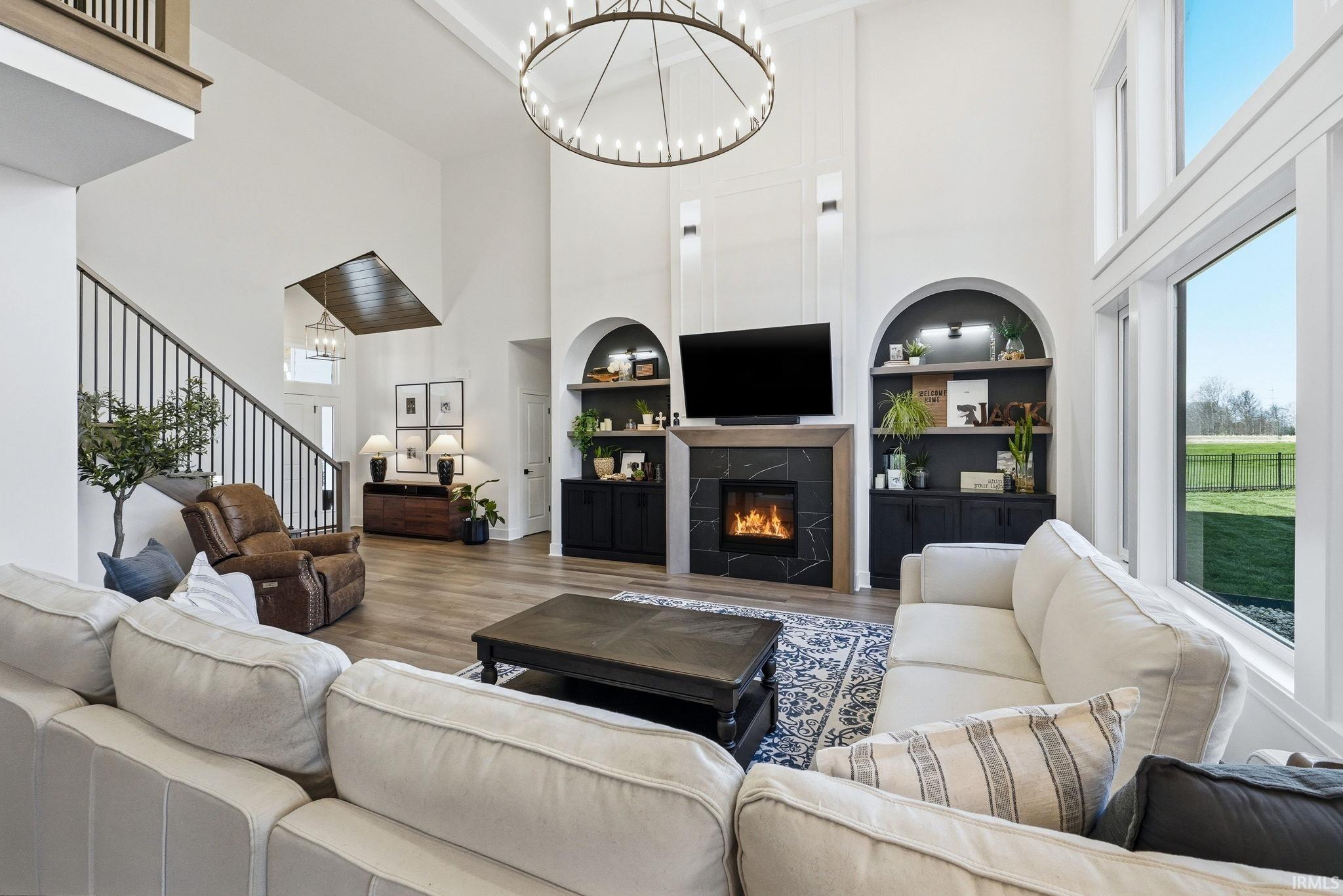 Living room featuring suspended lighting, a high ceiling, wood finished floors, a tile fireplace, and built in shelves