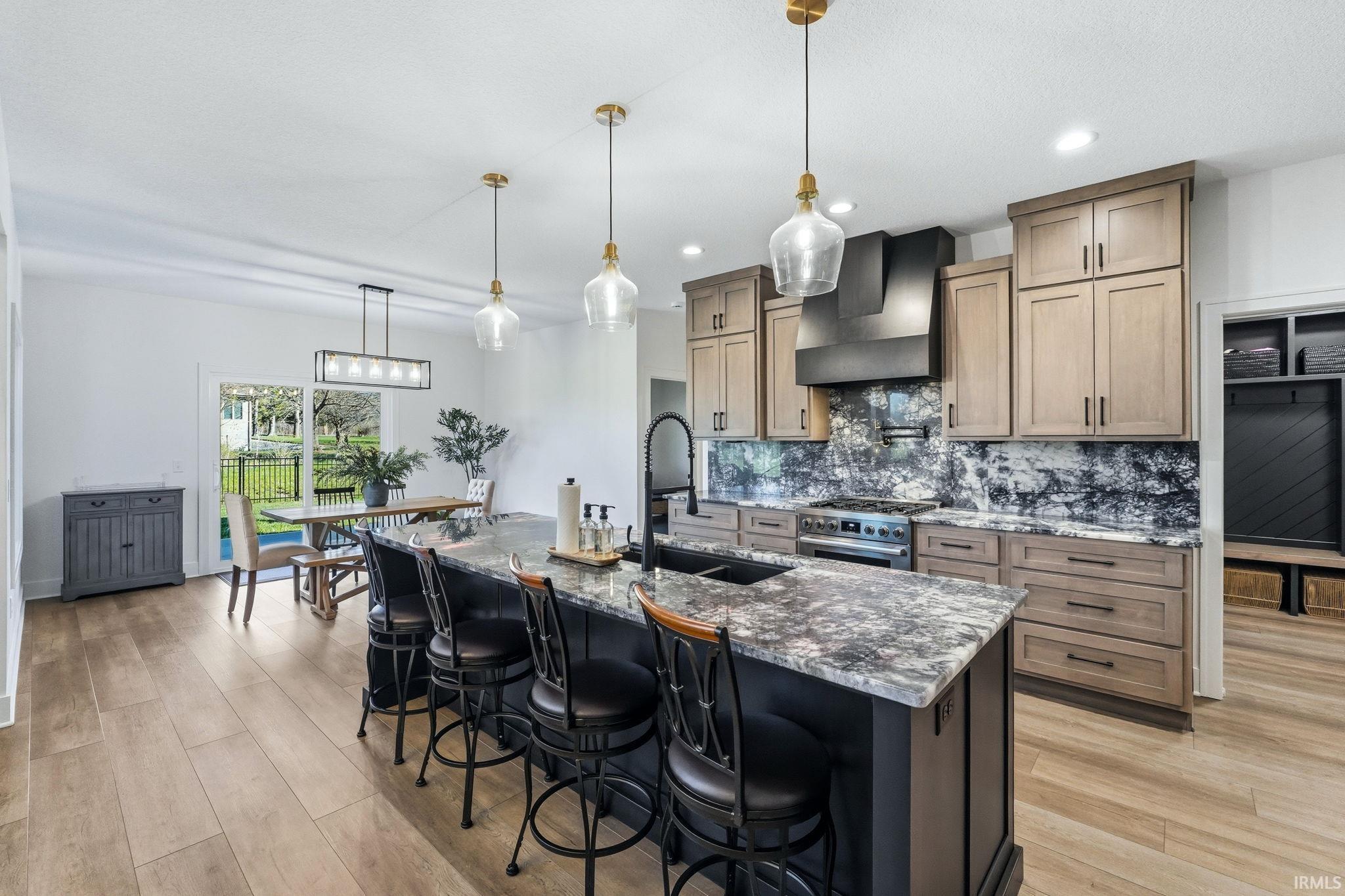 Dual tone kitchen with light wood-type flooring, a breakfast bar area, dark stone counters, decorative light fixtures, and stainless steel range