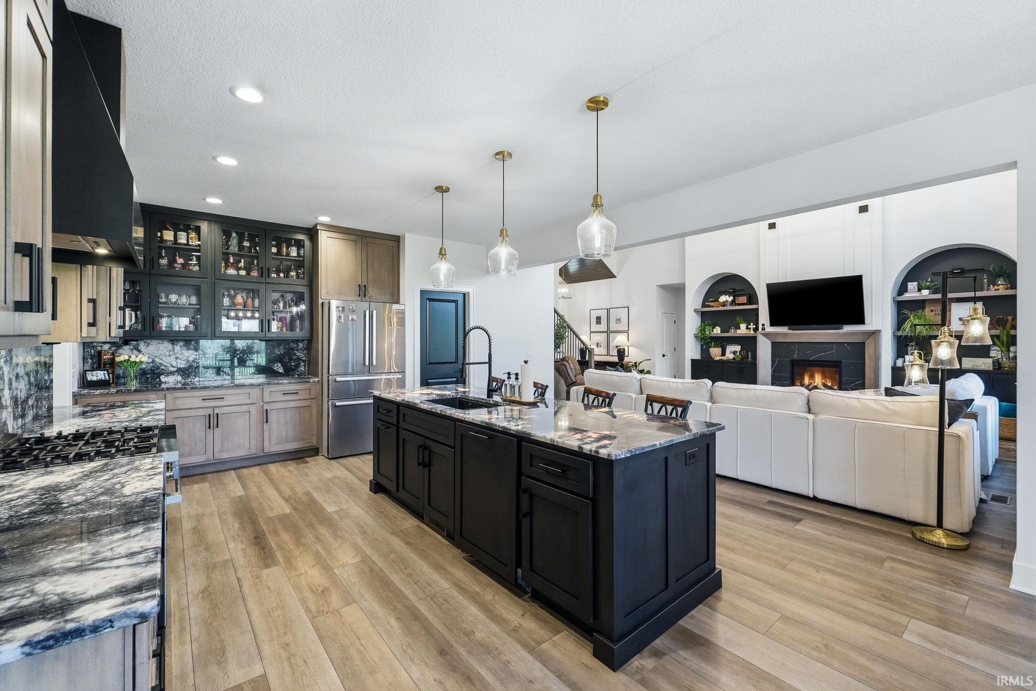 Two tone kitchen featuring glass insert cabinets, stainless steel appliances, two tone cabinets, dark stone countertops, and hanging light fixtures