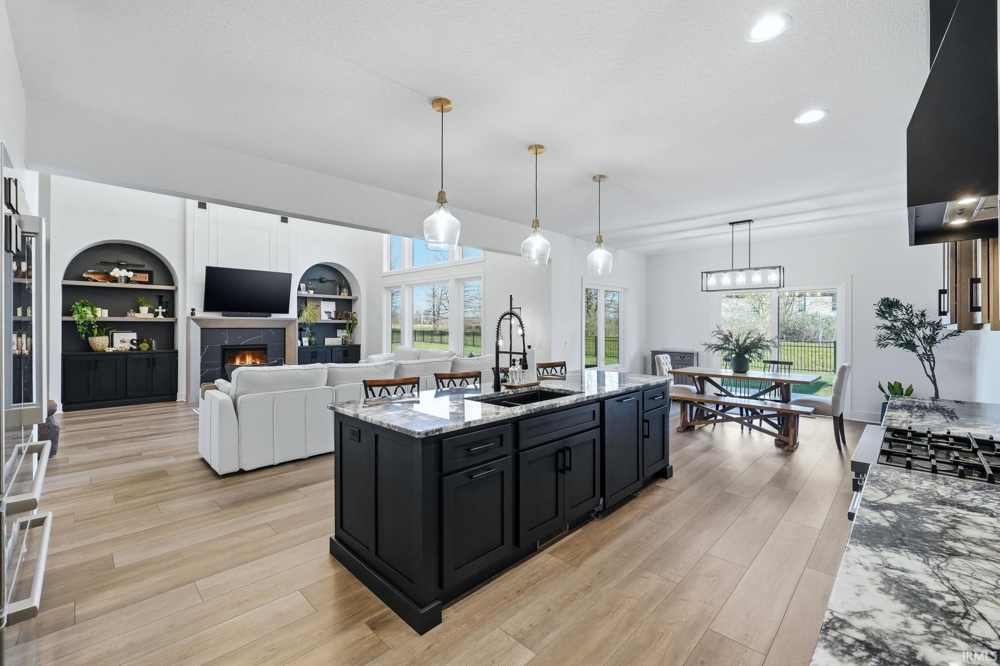Kitchen featuring dark cabinetry, light stone countertops, open floor plan, light wood-style floors, and hanging light fixtures