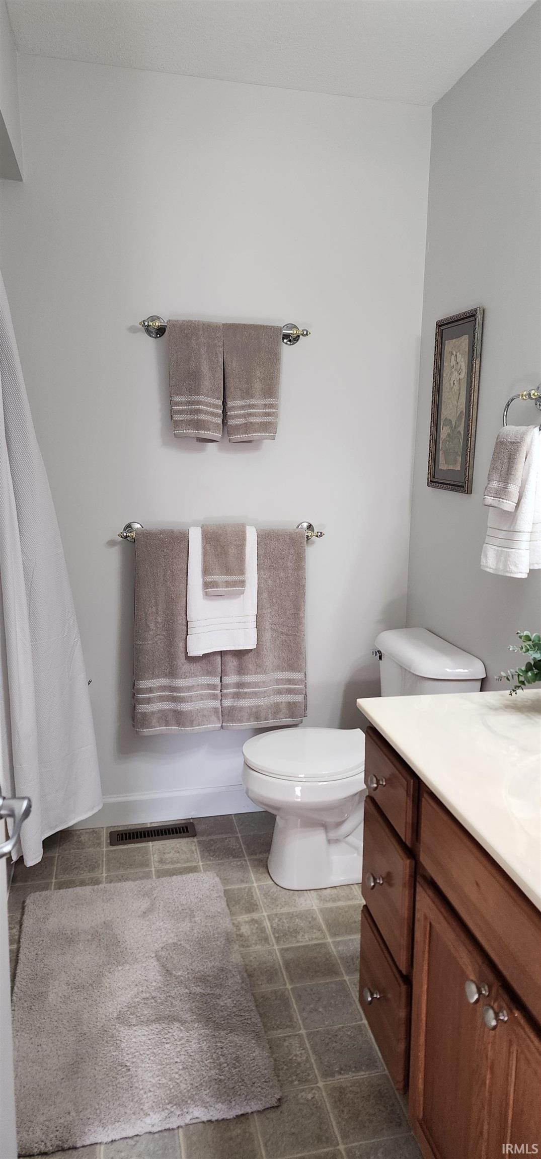 Bathroom featuring a wood-finish vanity with a light-toned countertop, square tile flooring, and light-colored walls