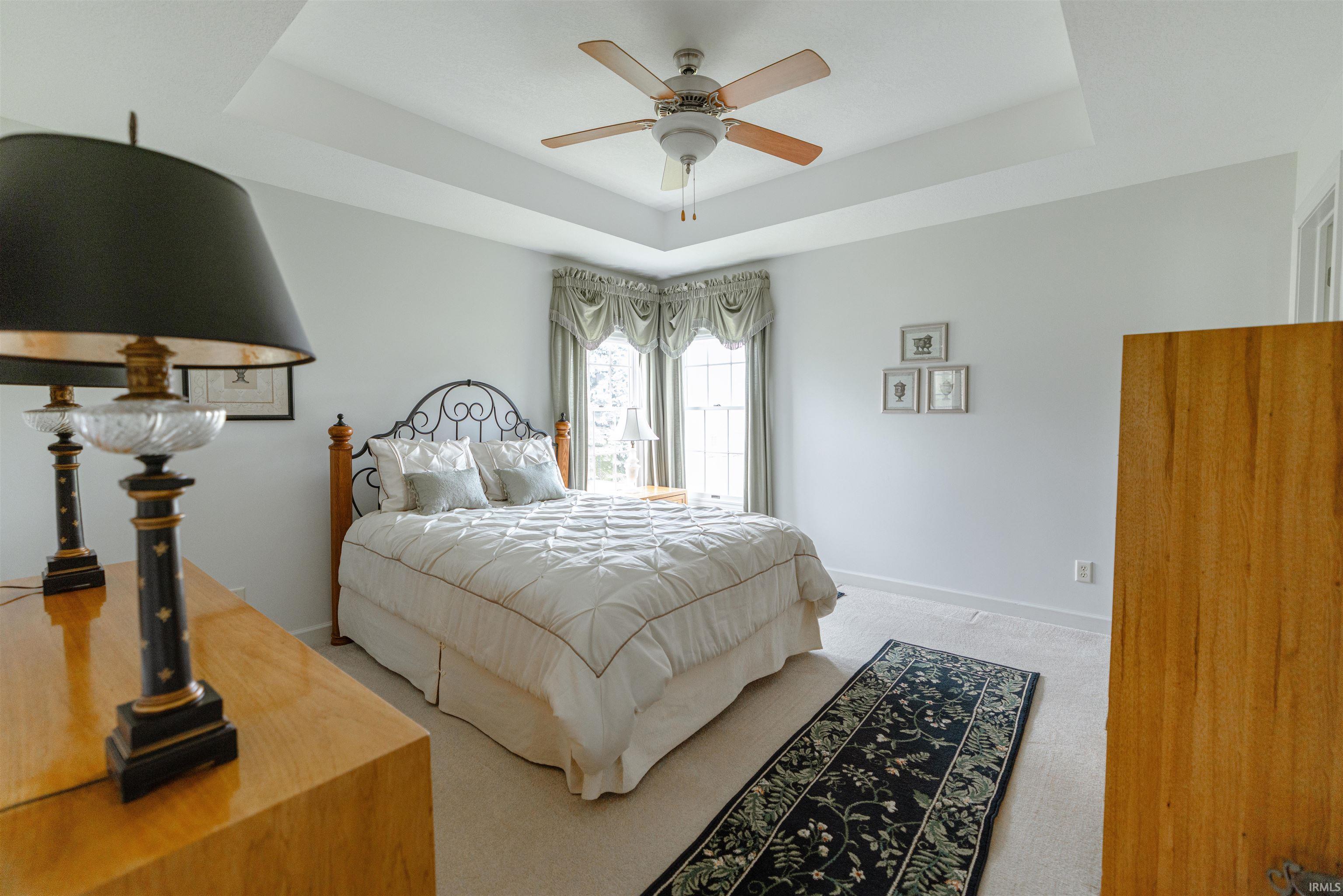 Bedroom with a raised ceiling, light carpet, and a ceiling fan