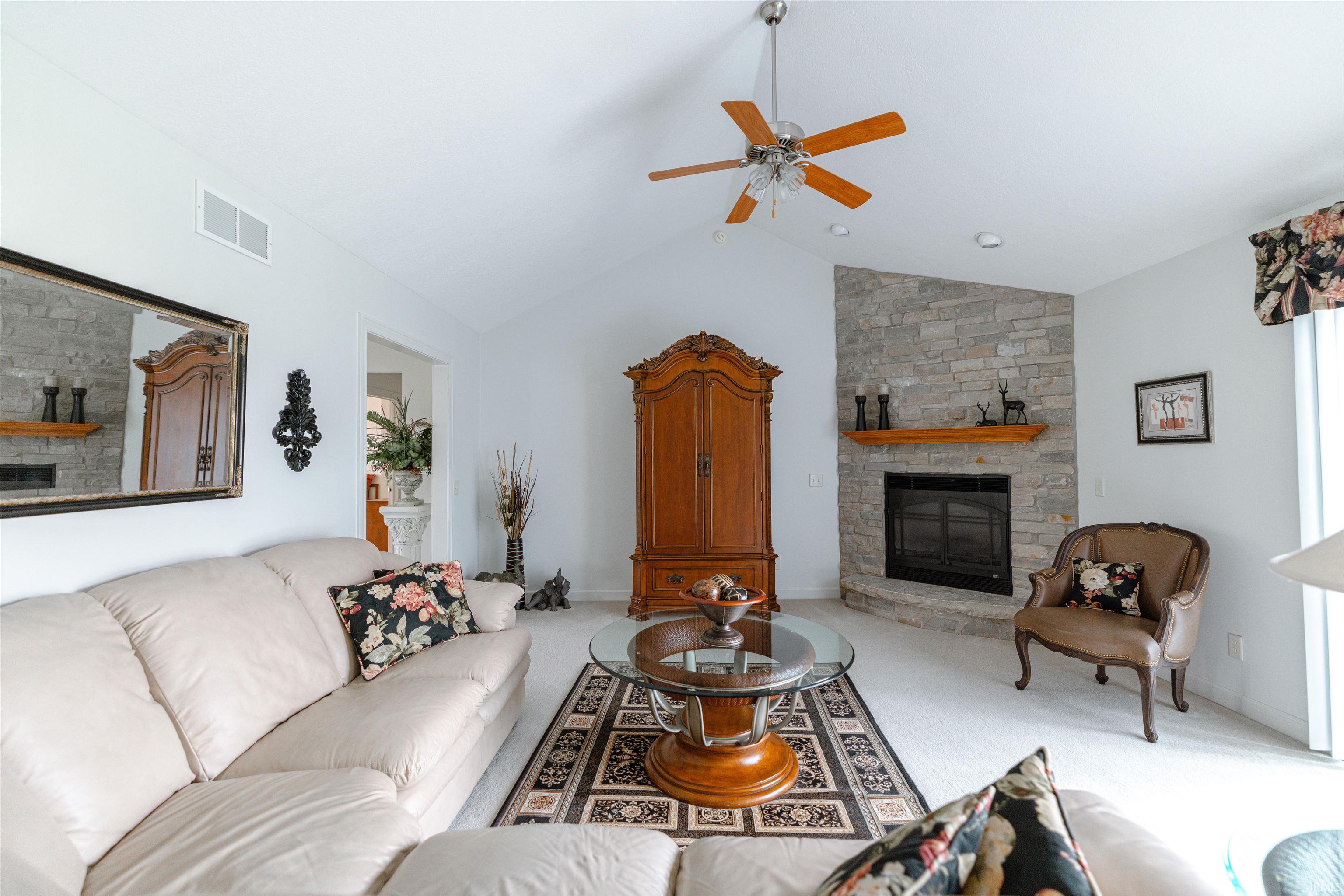 Living area featuring a stone fireplace, carpet floors, lofted ceiling, and a ceiling fan