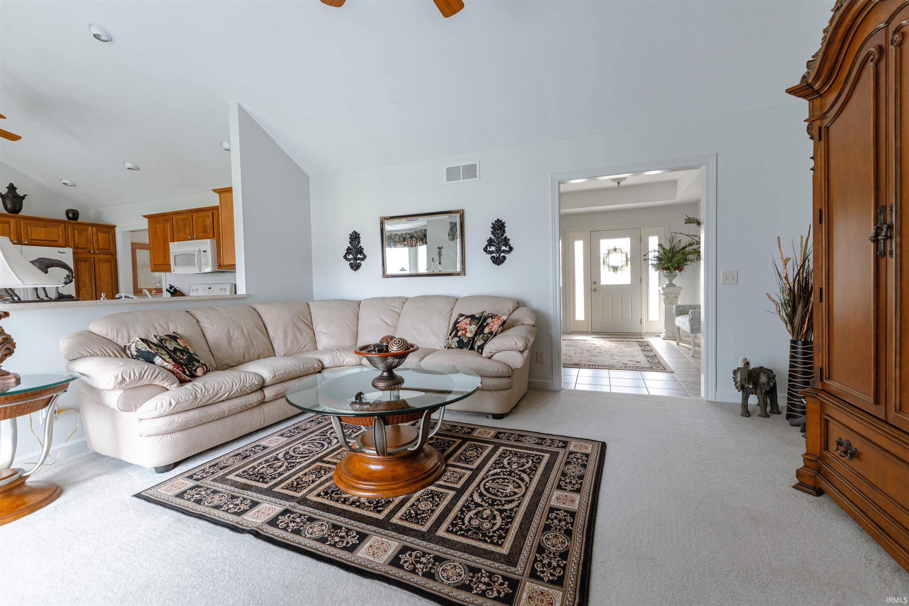 Living area with ceiling fan, light colored carpet, and vaulted ceiling