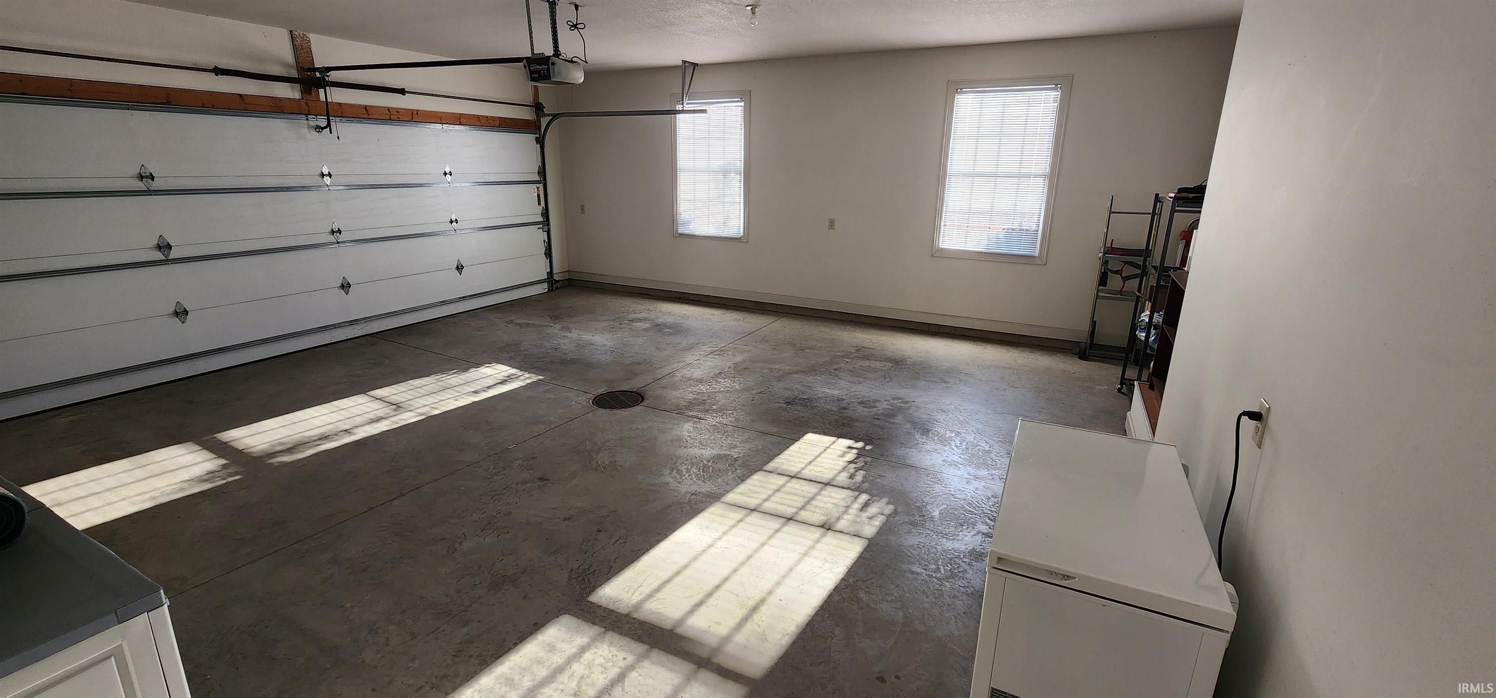 Spacious garage featuring a concrete floor, two windows providing natural light, and an automatic overhead door