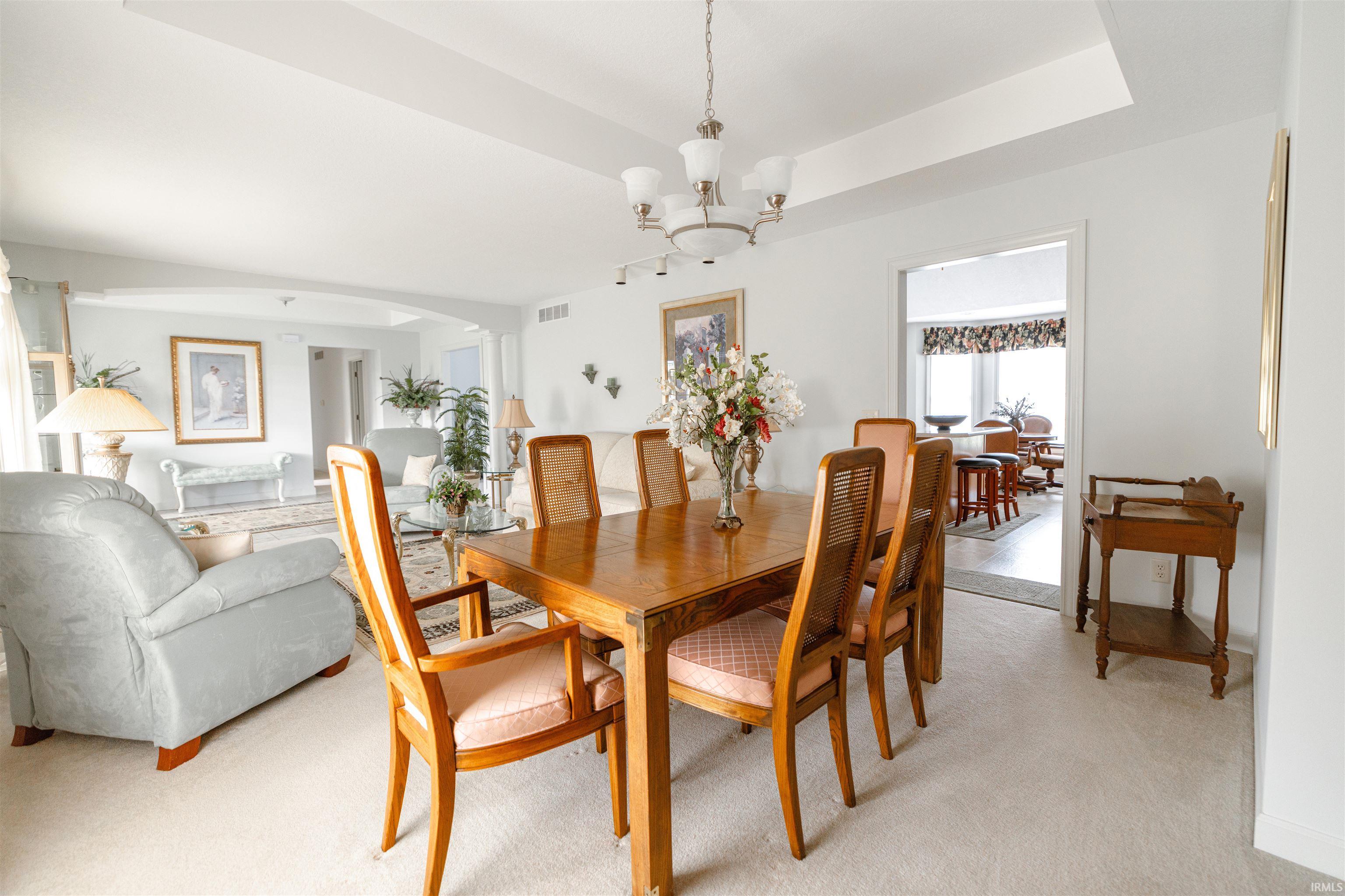 Dining space with arched walkways, suspended lighting, a raised ceiling, and light carpet