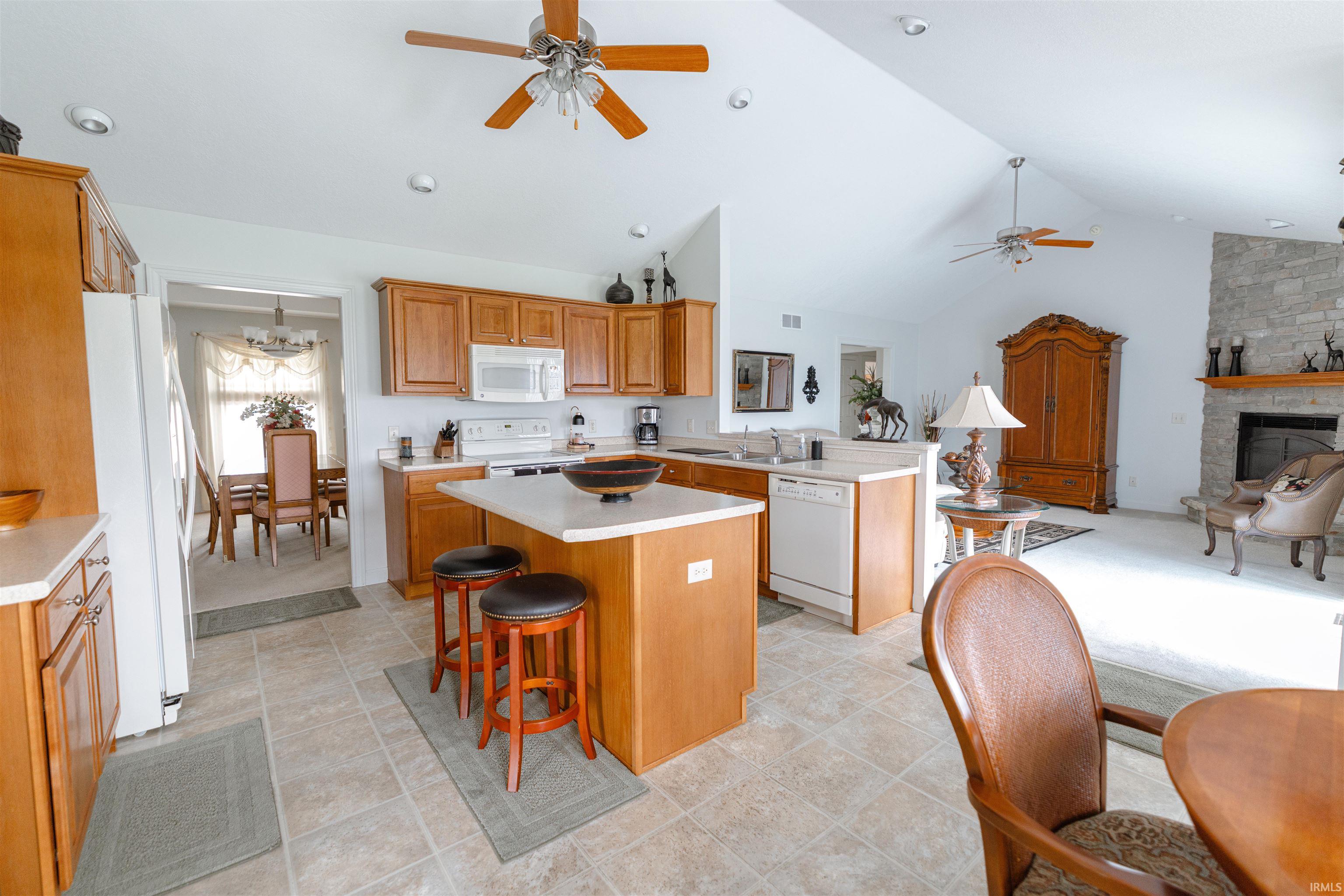 Kitchen with ceiling fan, a kitchen breakfast bar, light countertops, white appliances, and wood finish cabinets