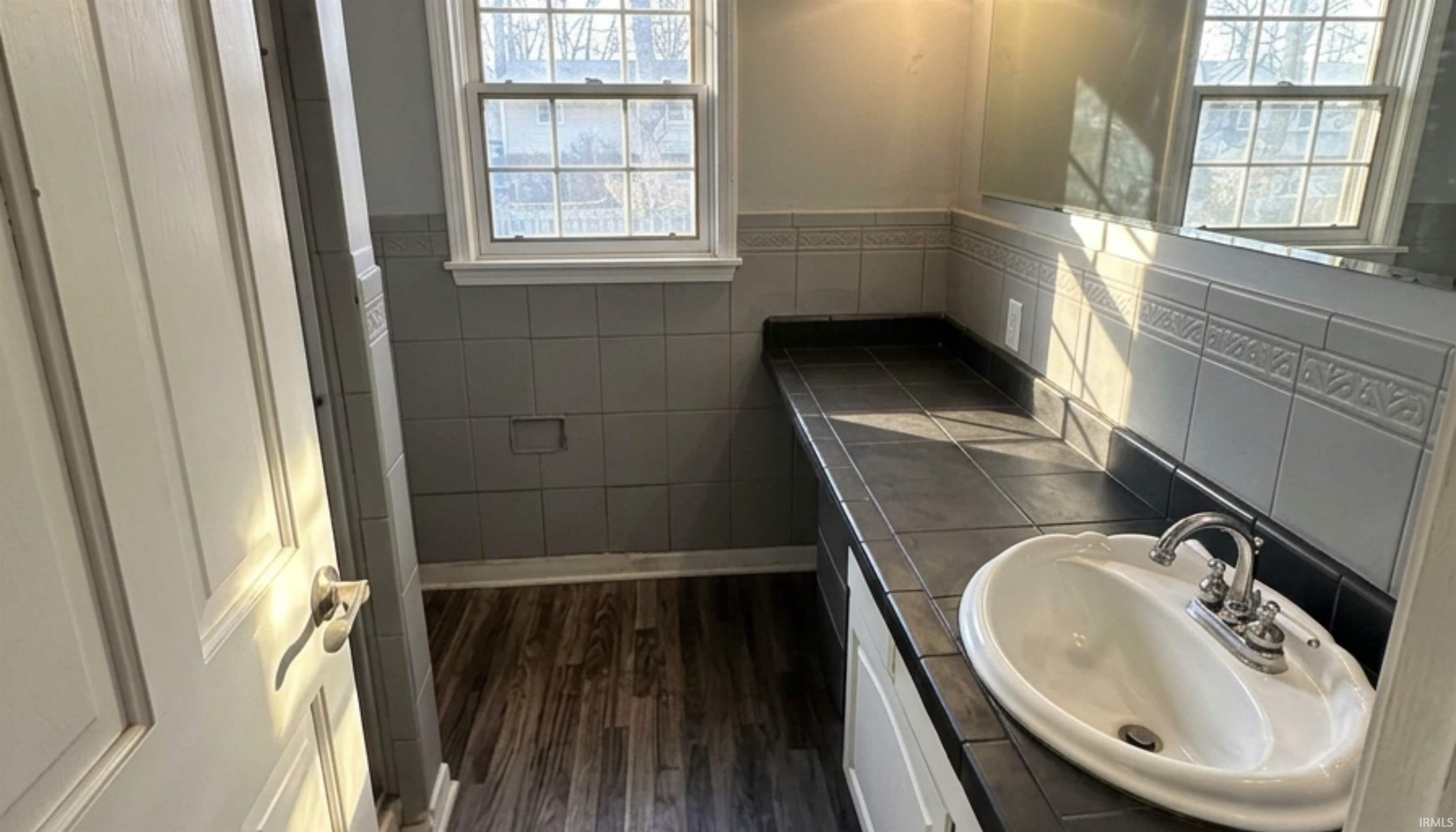 Full bath featuring wood-type flooring, tile countertop, vanity, and stand-up shower.