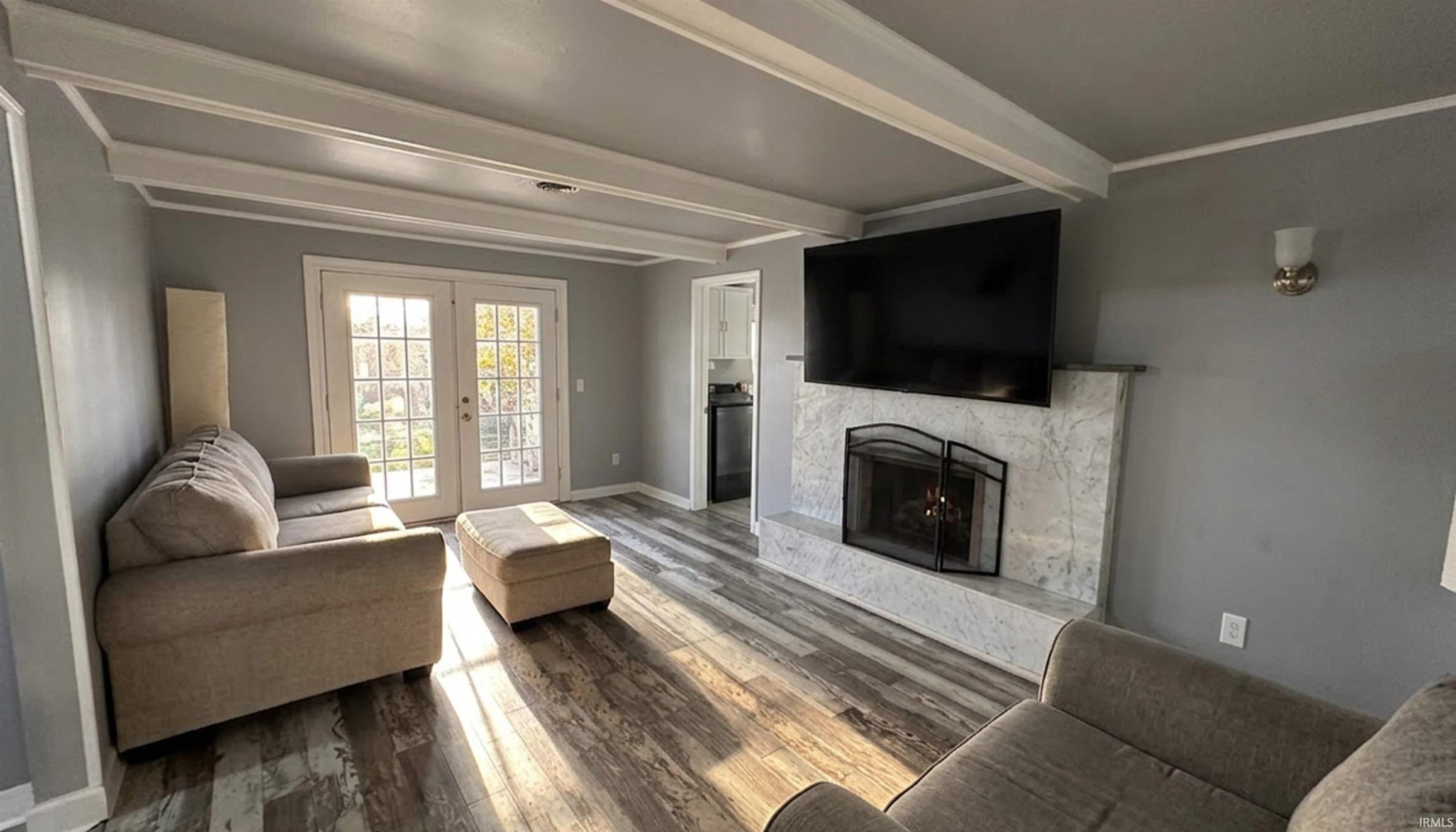 Living room with french doors that lead to the Florida room. Wood flooring, a ventless gas-fireplace to help with heating costs in the colder seasons, and beautiful beamed ceiling. (AI Generated staging)