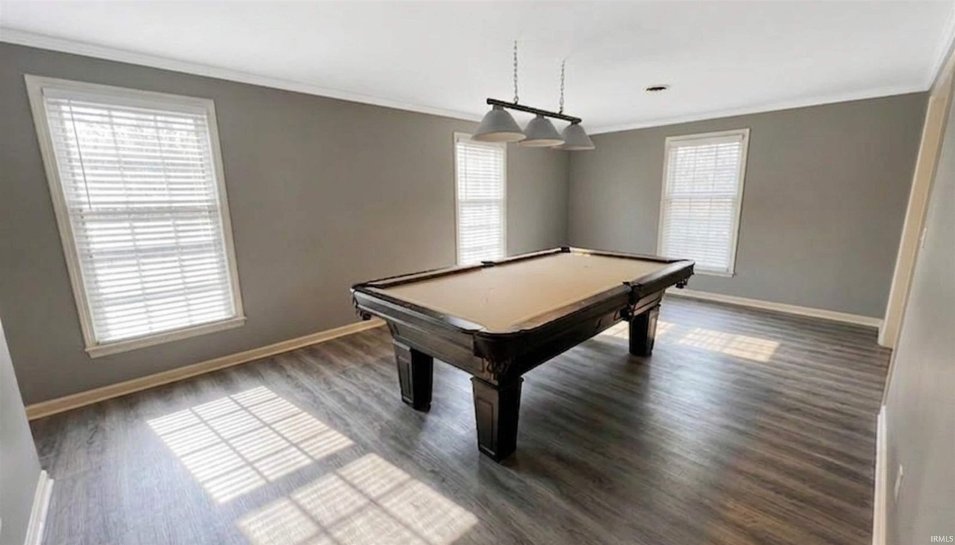 Living room with ornamental molding, pool table, ping-pong table (not pictured), and wood flooring. (AI Generated staging)