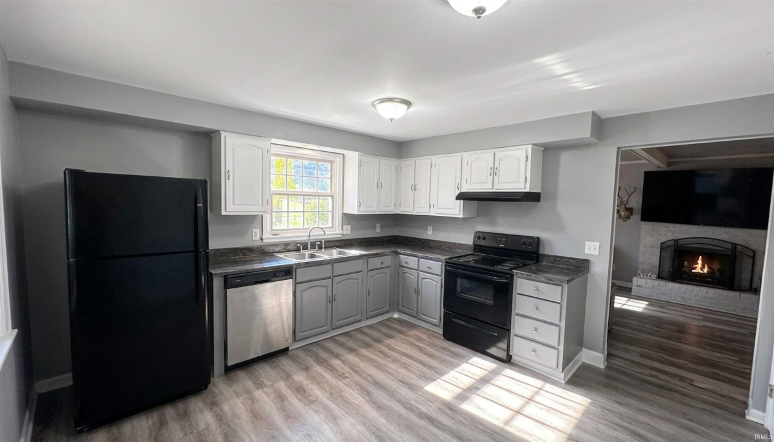 Kitchen with dark countertops, black appliances, wood flooring. (AI Generated staging)