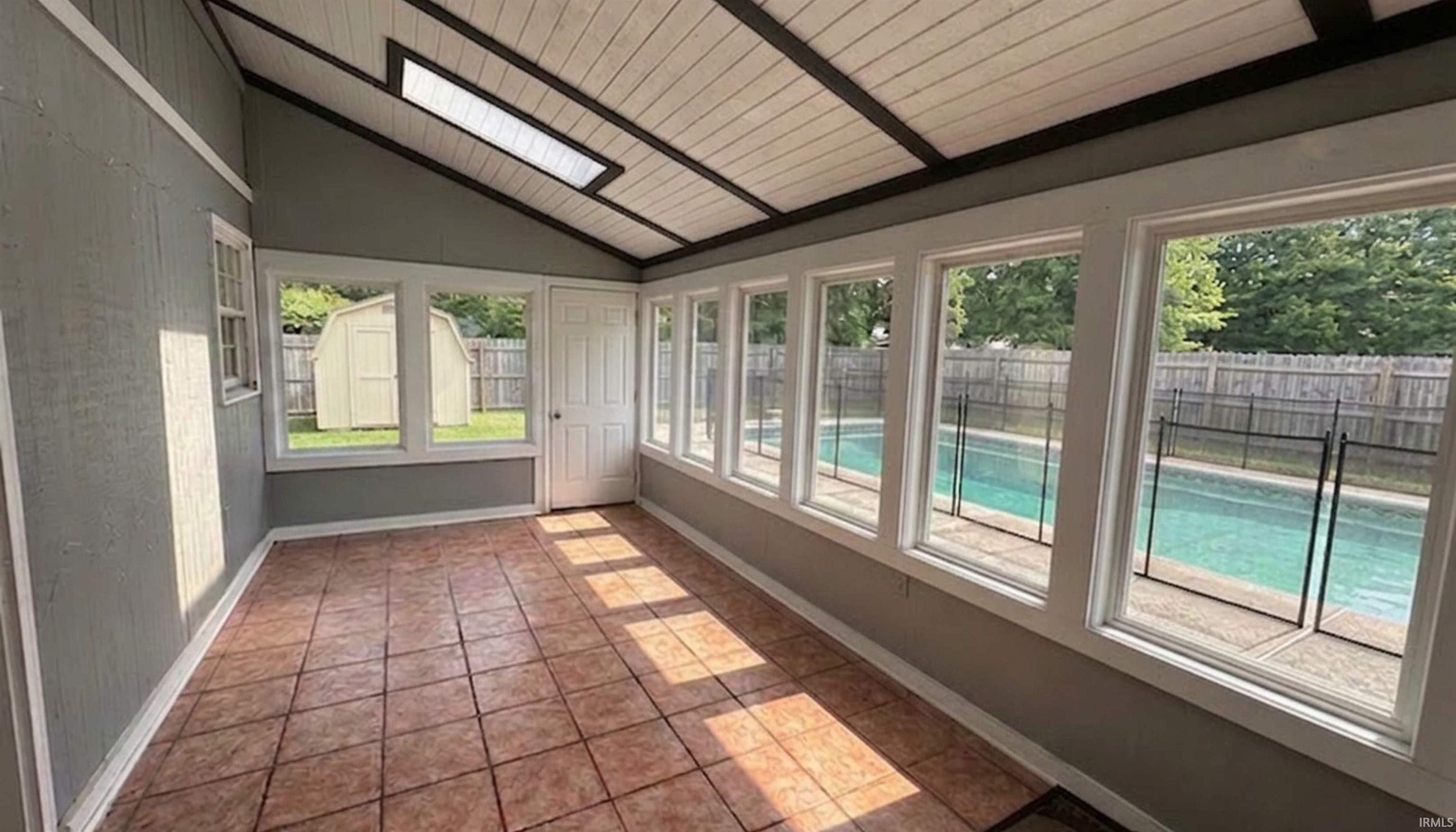 Florida sunroom featuring ceramic tile flooring, healthy amount of natural light, and a vaulted wooden ceiling, with a view of the backyard and in-ground pool. (AI Generated staging)