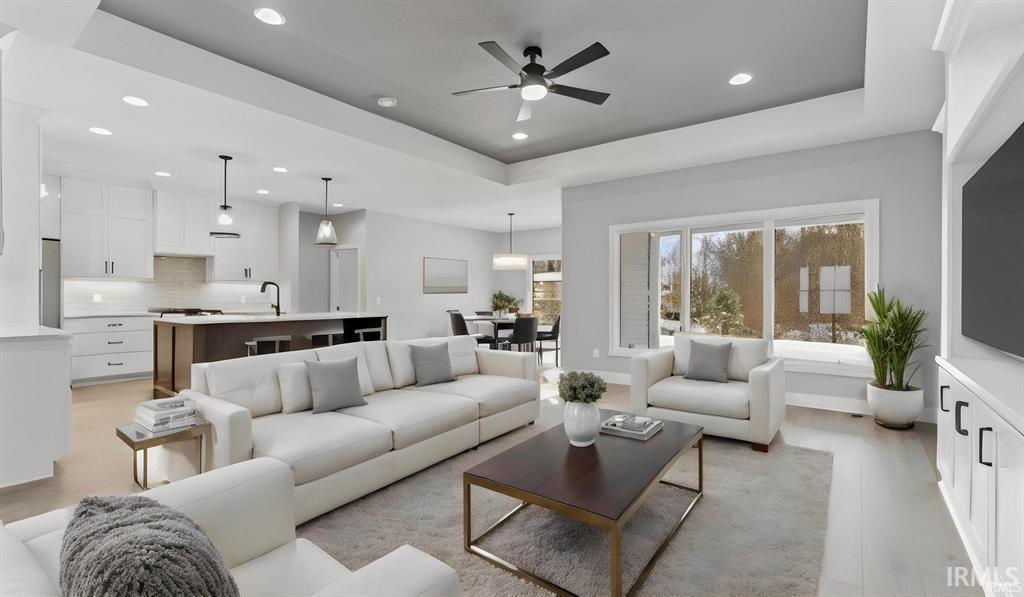 Living room featuring a tray ceiling, ceiling fan, light wood-style flooring, and recessed lighting