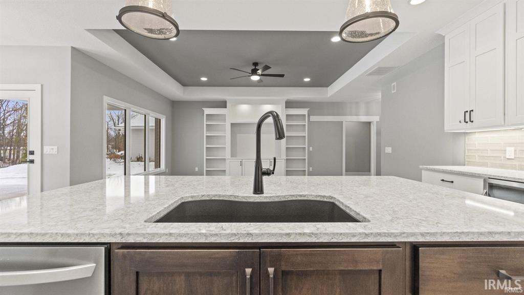 Kitchen with a raised ceiling, light stone counters, tasteful backsplash, recessed lighting, and stainless steel dishwasher