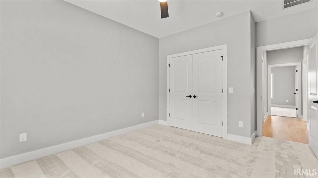Unfurnished bedroom with light colored carpet, a closet, and a ceiling fan