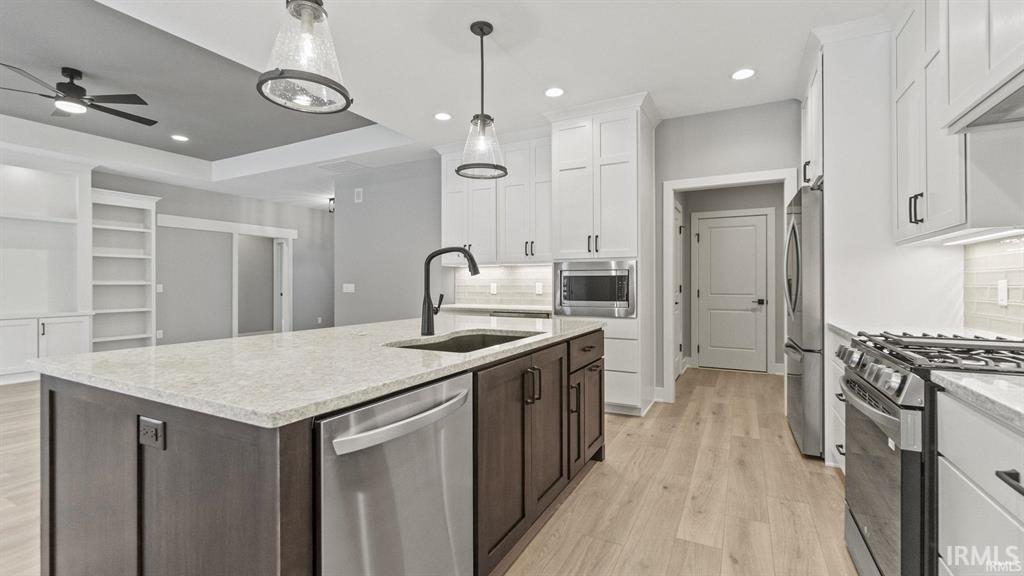 Two tone kitchen featuring stainless steel appliances, tasteful backsplash, a kitchen island with sink, light stone counters, and two tone color scheme