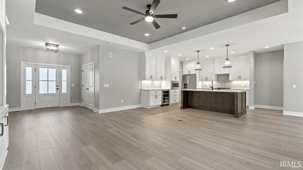 Dual tone kitchen with open floor plan, a tray ceiling, ceiling fan, light countertops, and a kitchen island with sink