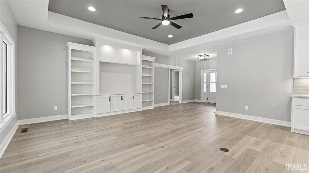 Unfurnished living room with a raised ceiling, ceiling fan, recessed lighting, and light wood finished floors