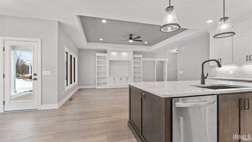 Kitchen featuring a raised ceiling, stainless steel dishwasher, light stone counters, tasteful backsplash, and a ceiling fan