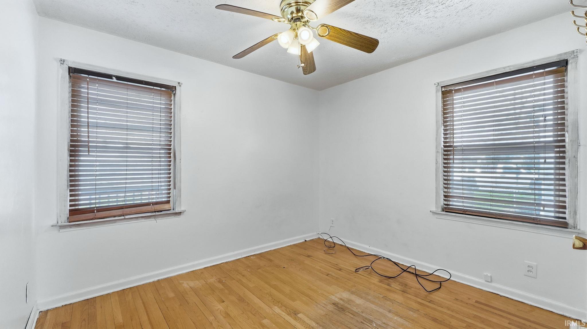 Empty room featuring light wood-style flooring, a ceiling fan, and a textured ceiling