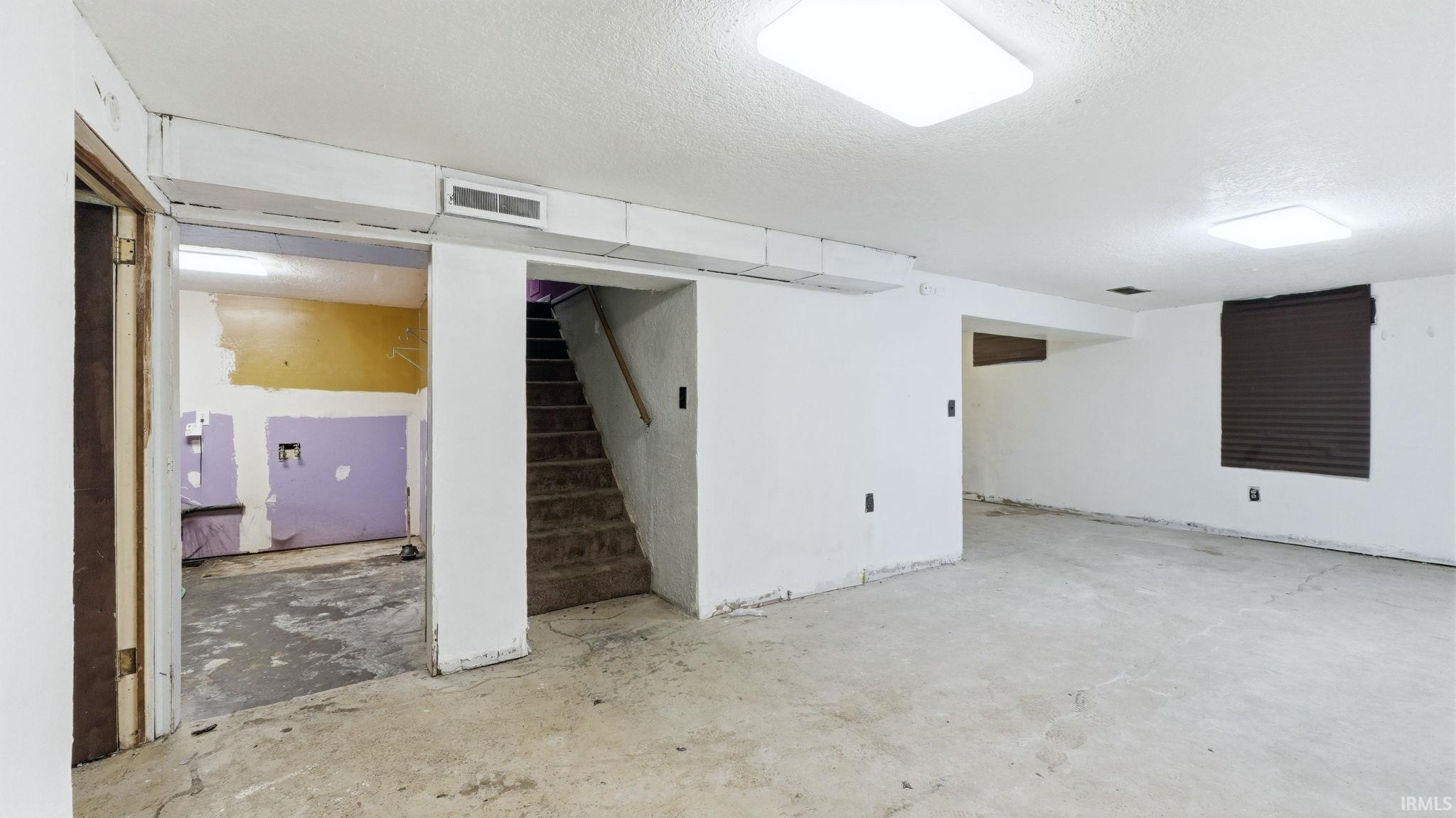 Finished basement featuring a textured ceiling and stairs