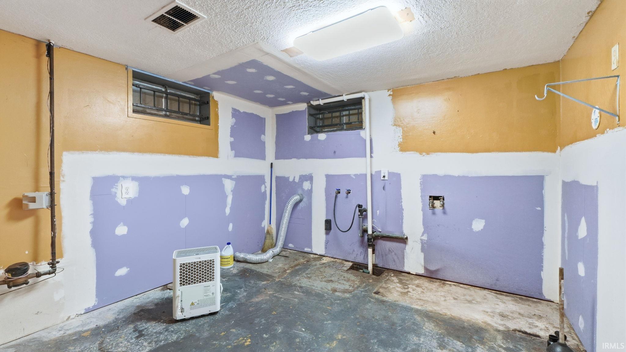 Laundry area featuring a textured ceiling and unfinished concrete flooring
