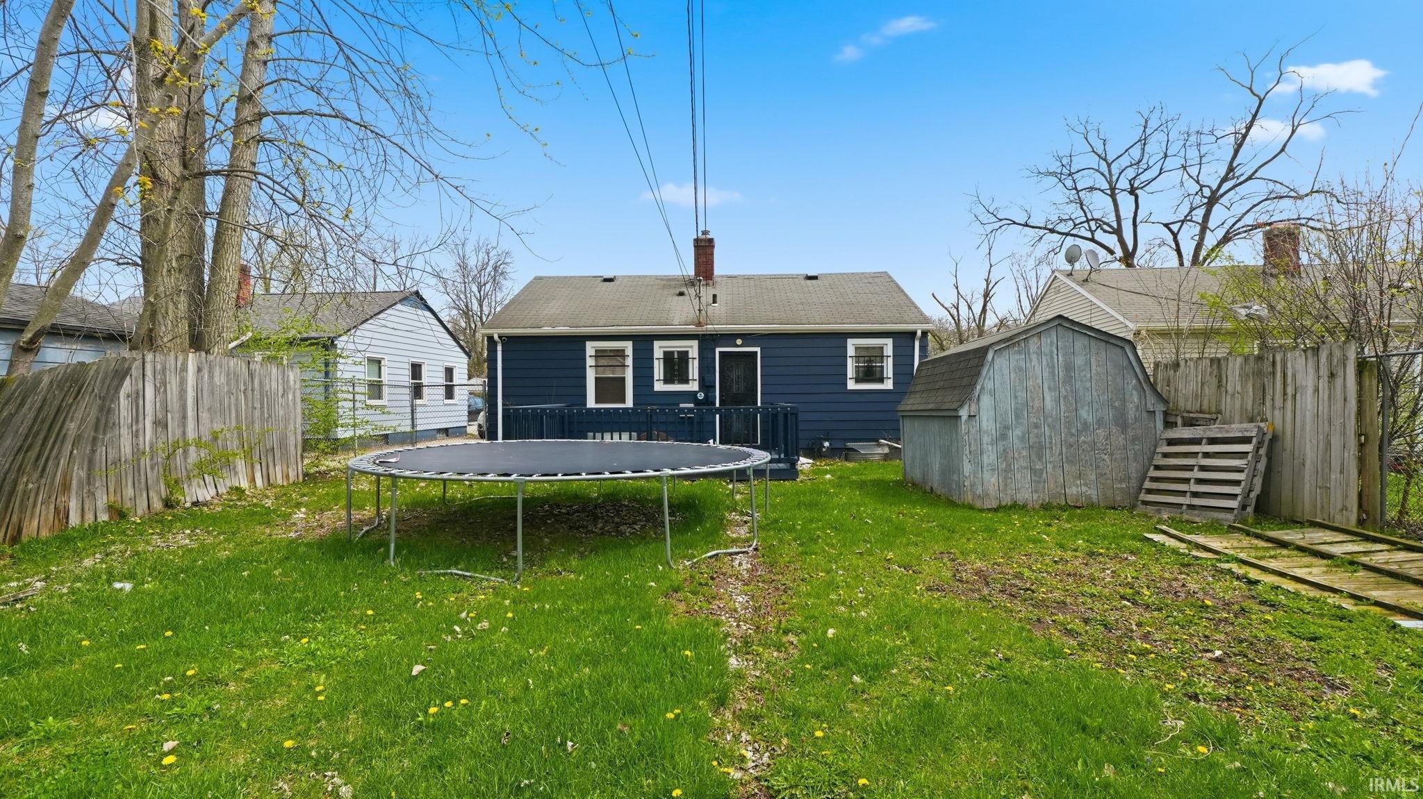Rear view of property featuring a shed, a trampoline, a fenced backyard, a chimney, and a wooden deck