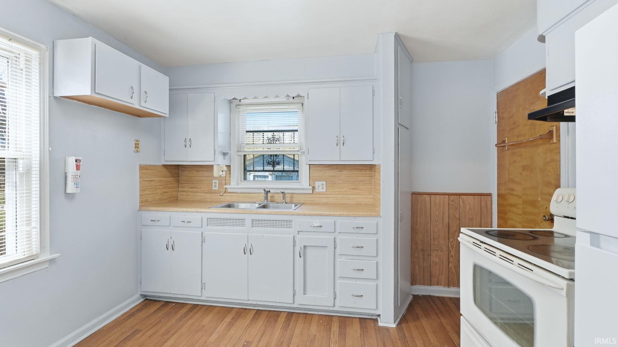 Kitchen with white appliances, white cabinets, light countertops, and light wood-style floors