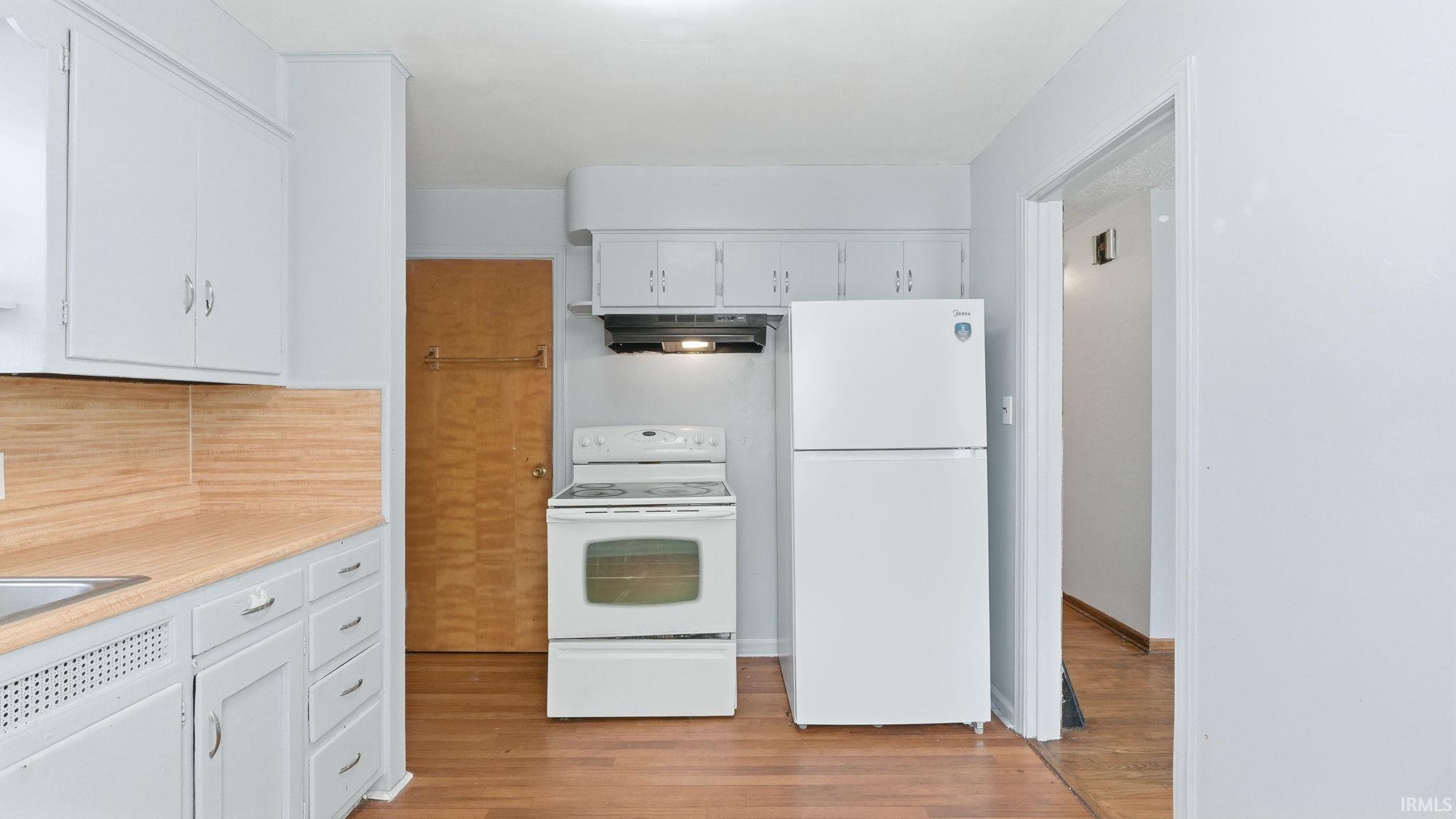 Kitchen featuring white appliances, light countertops, white cabinetry, light wood-type flooring, and backsplash