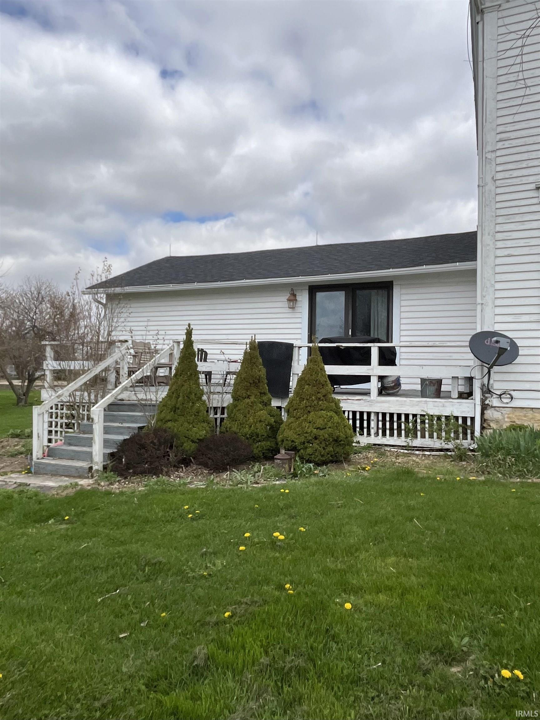 View of exterior entry with a yard, roof with shingles, and a wooden deck