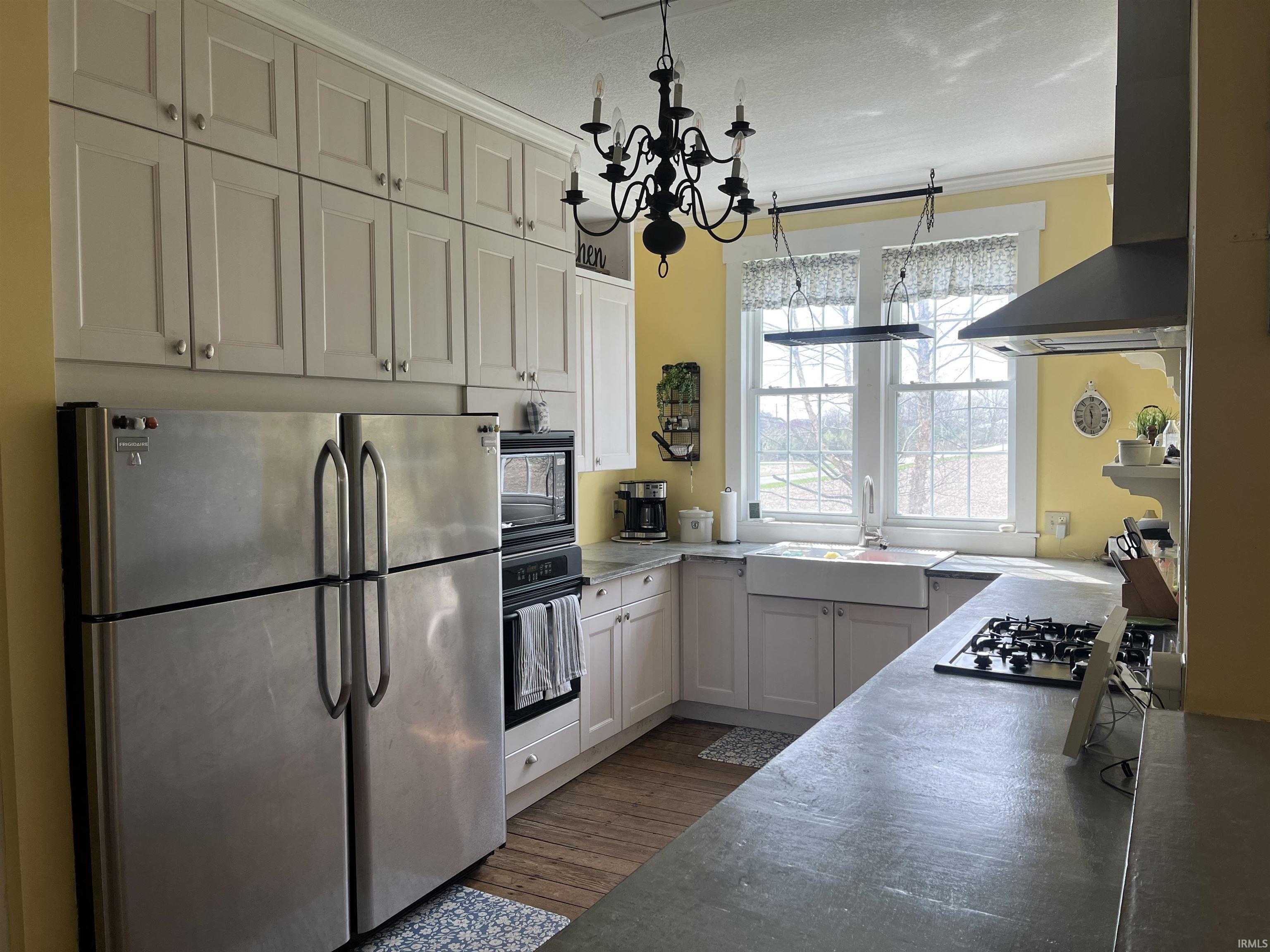 Kitchen with black appliances, range hood, ornamental molding, suspended lighting, and white cabinetry