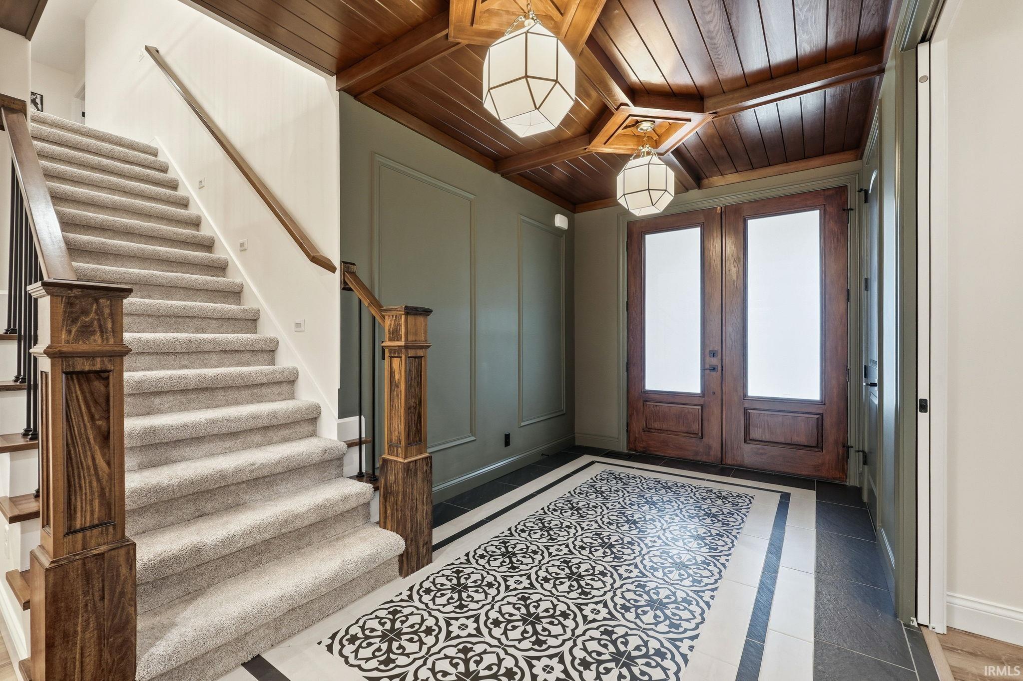 Foyer with inlaid floor details, wood ceiling, french doors, and a decorative wall