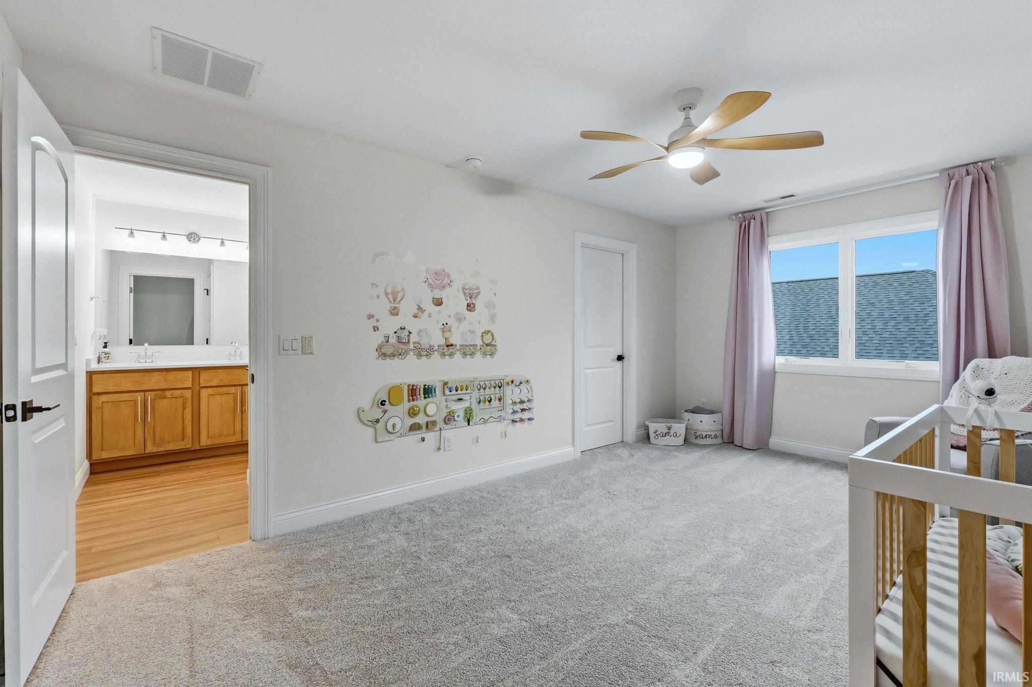 Unfurnished bedroom featuring light carpet, a nursery area, and ceiling fan