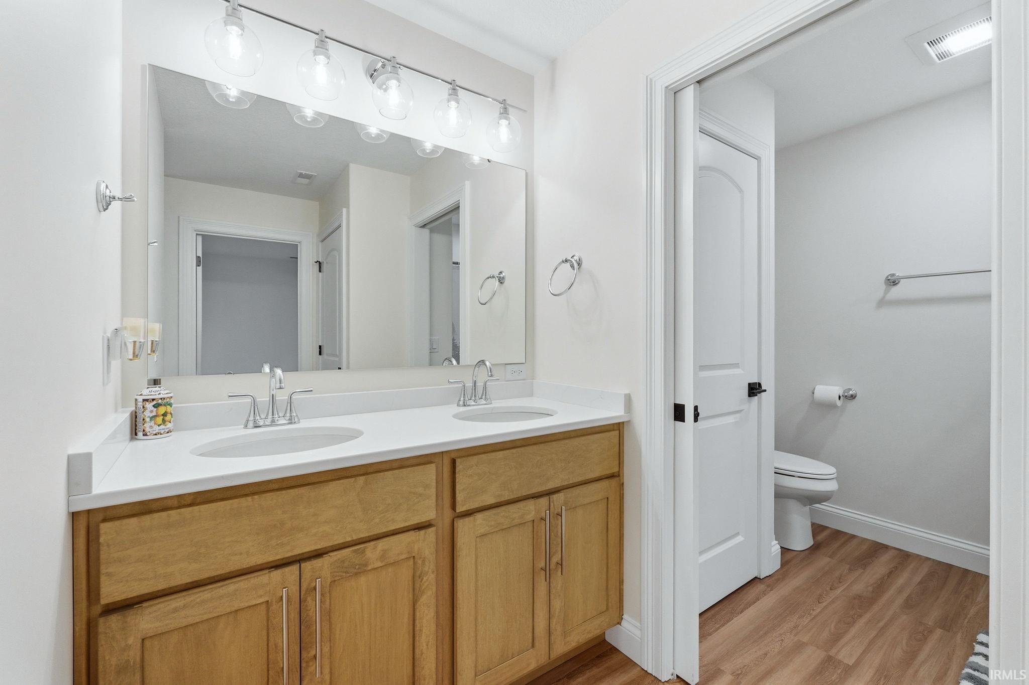 Full bath with double vanity and light wood-style flooring