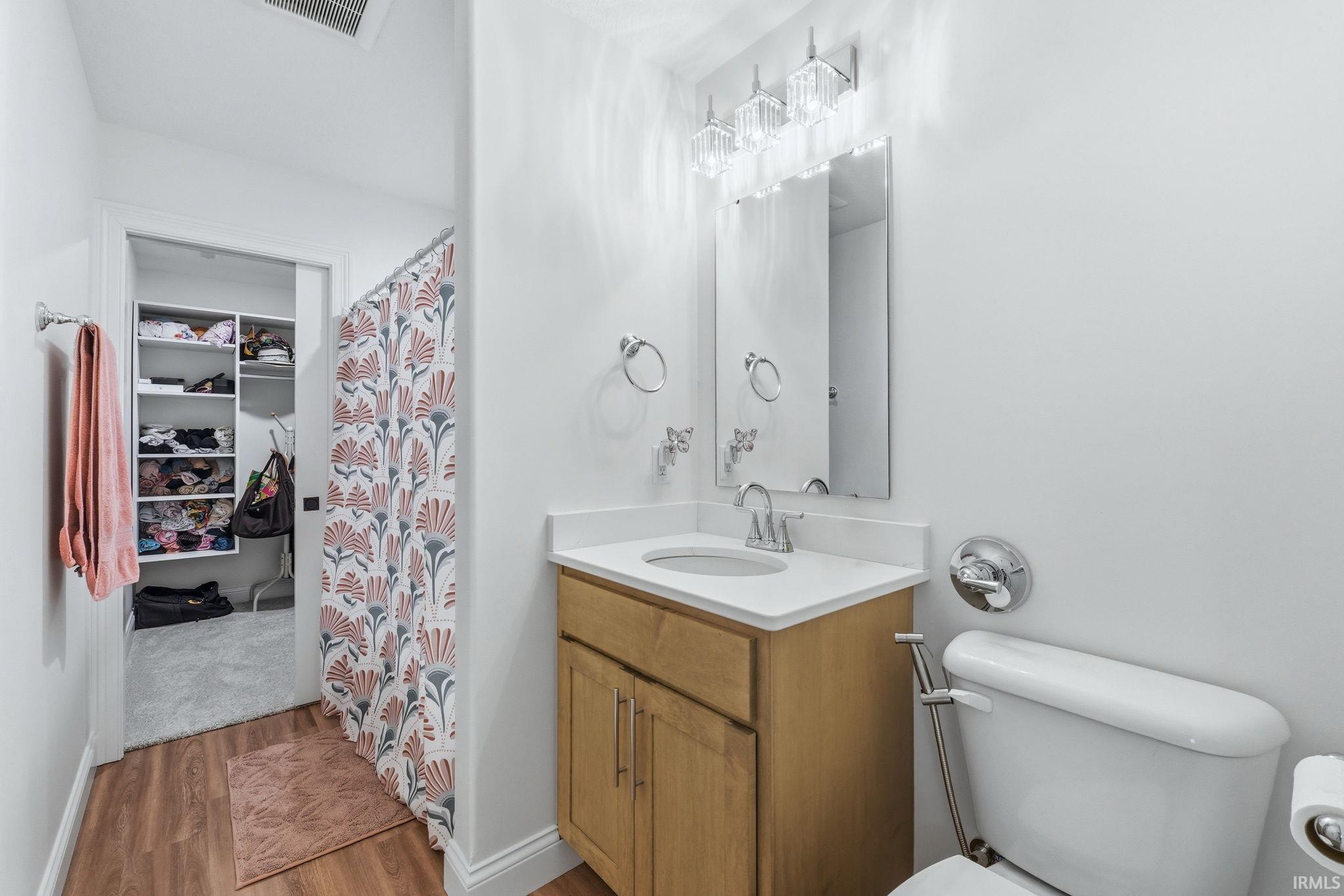 Full bath featuring a shower with shower curtain, vanity, light wood-style floors, and a spacious closet