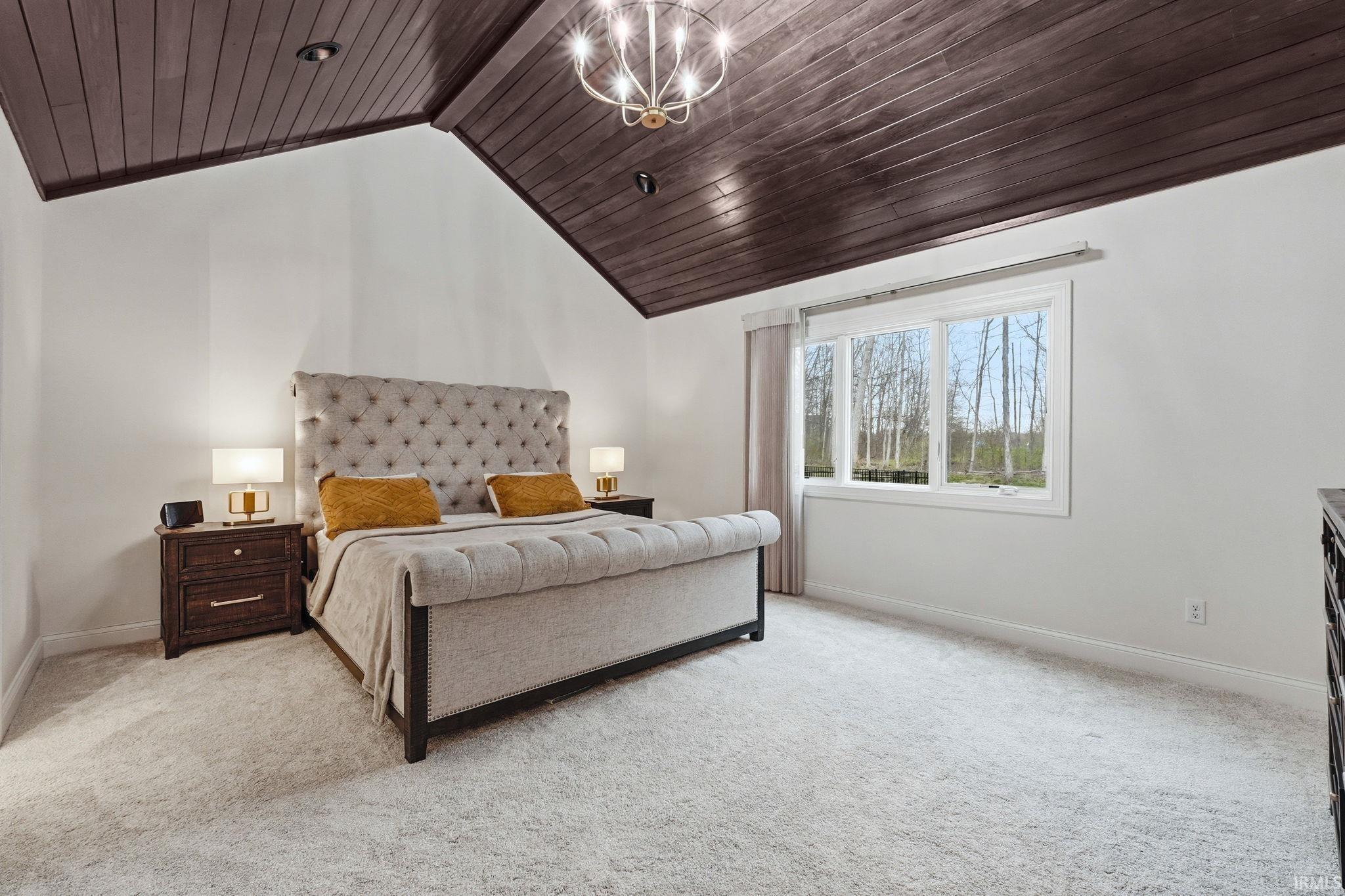 Bedroom with a high wooden beamed ceiling, light colored carpet, and suspended lighting