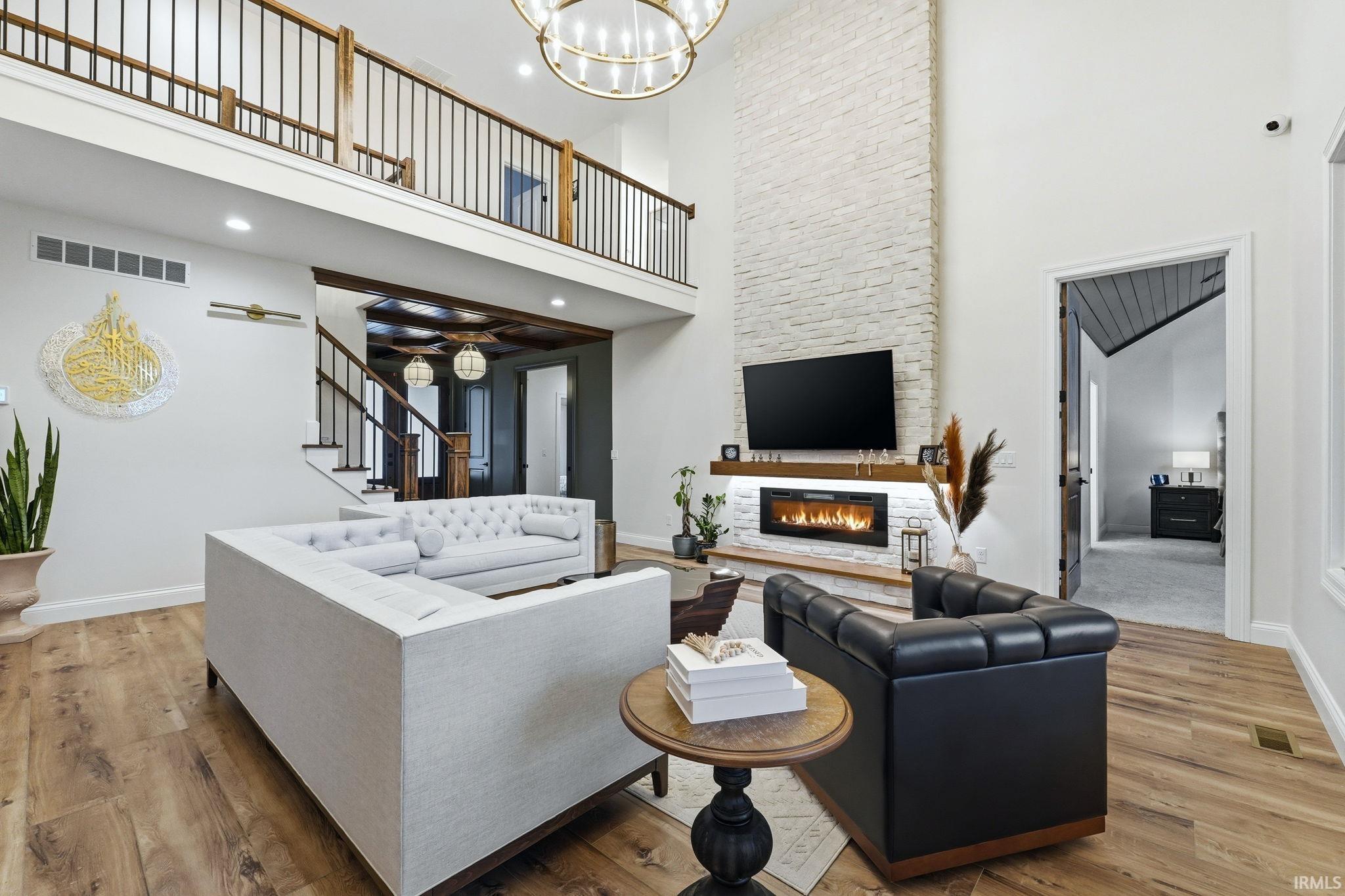 Living room with wood finished floors, suspended lighting, a fireplace, and a high ceiling
