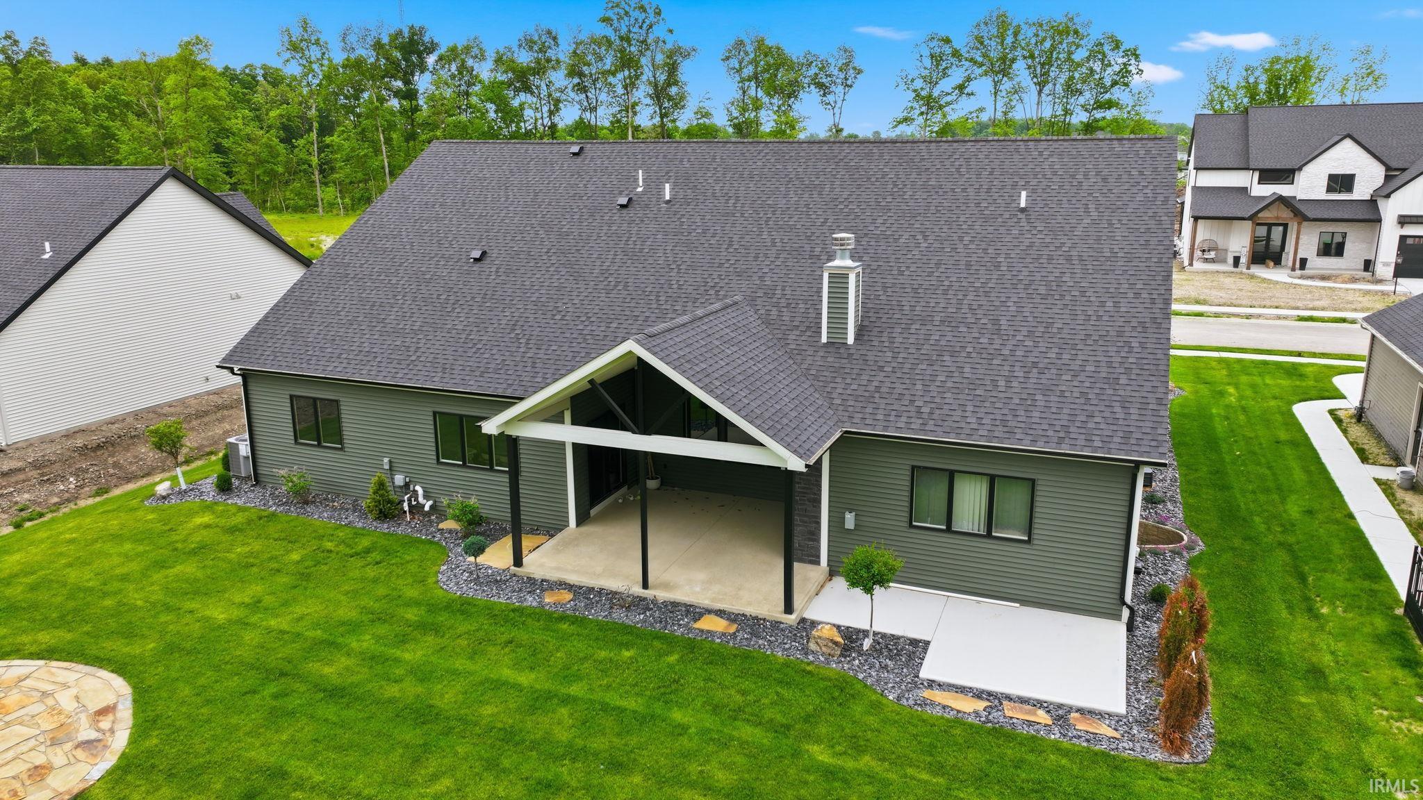 Rear exterior with covered patio, dark gray shingle roof, green horizontal siding, and multiple windows
