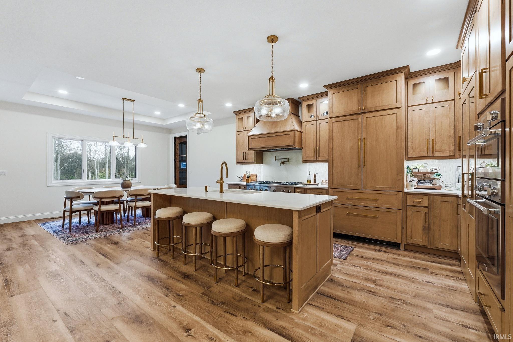 Kitchen with a breakfast bar, a kitchen island with sink, wood finish cabinets, pendant lighting, and a raised ceiling