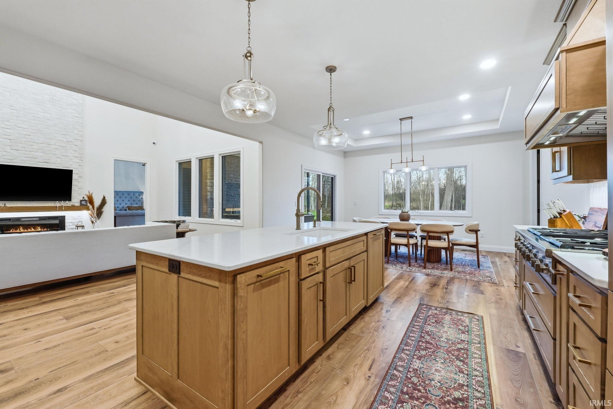 Kitchen featuring open floor plan, a kitchen island with sink, wood finish cabinetry, decorative light fixtures, and light wood finished floors