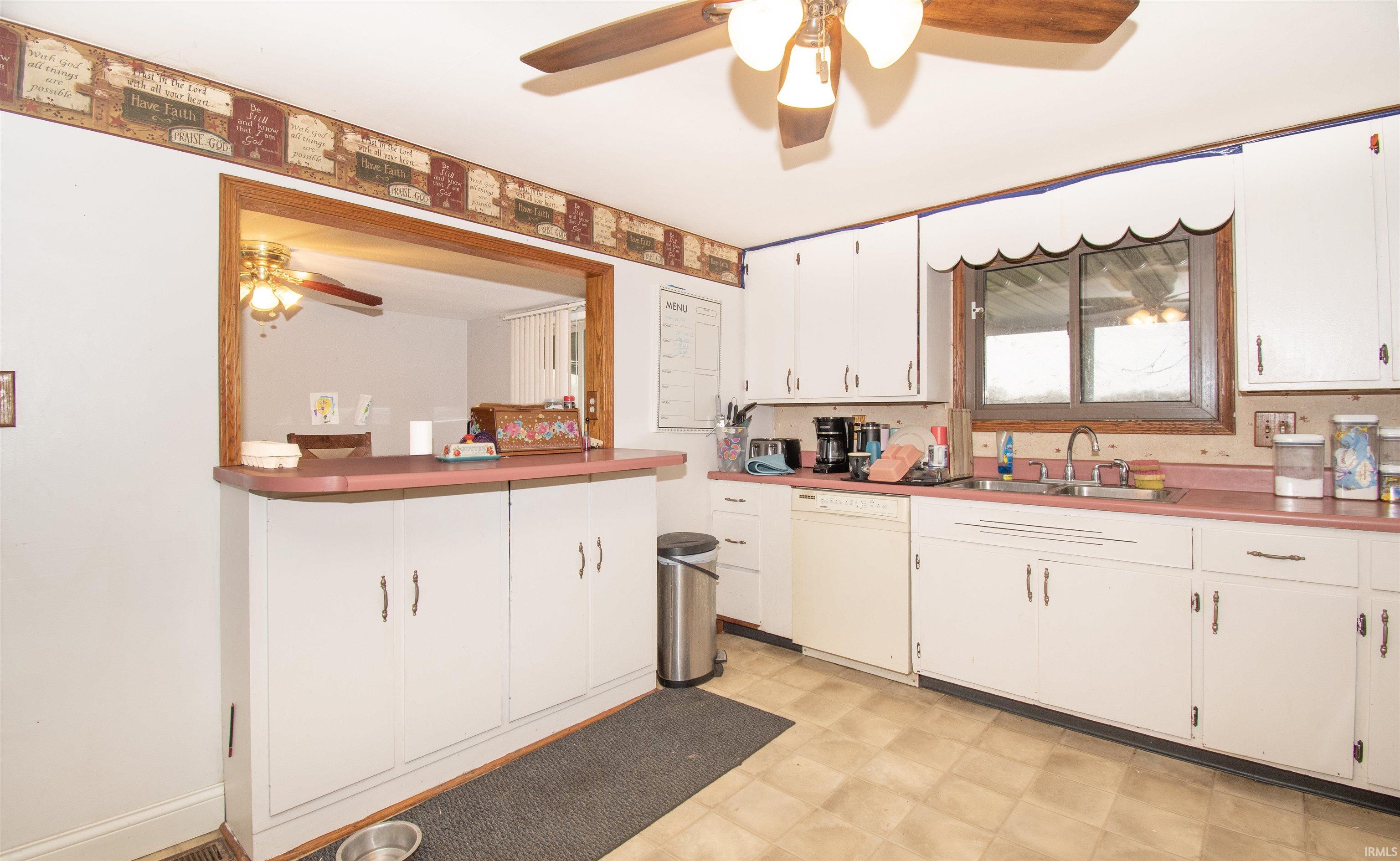 Kitchen featuring a ceiling fan, light flooring, white cabinets, and white dishwasher