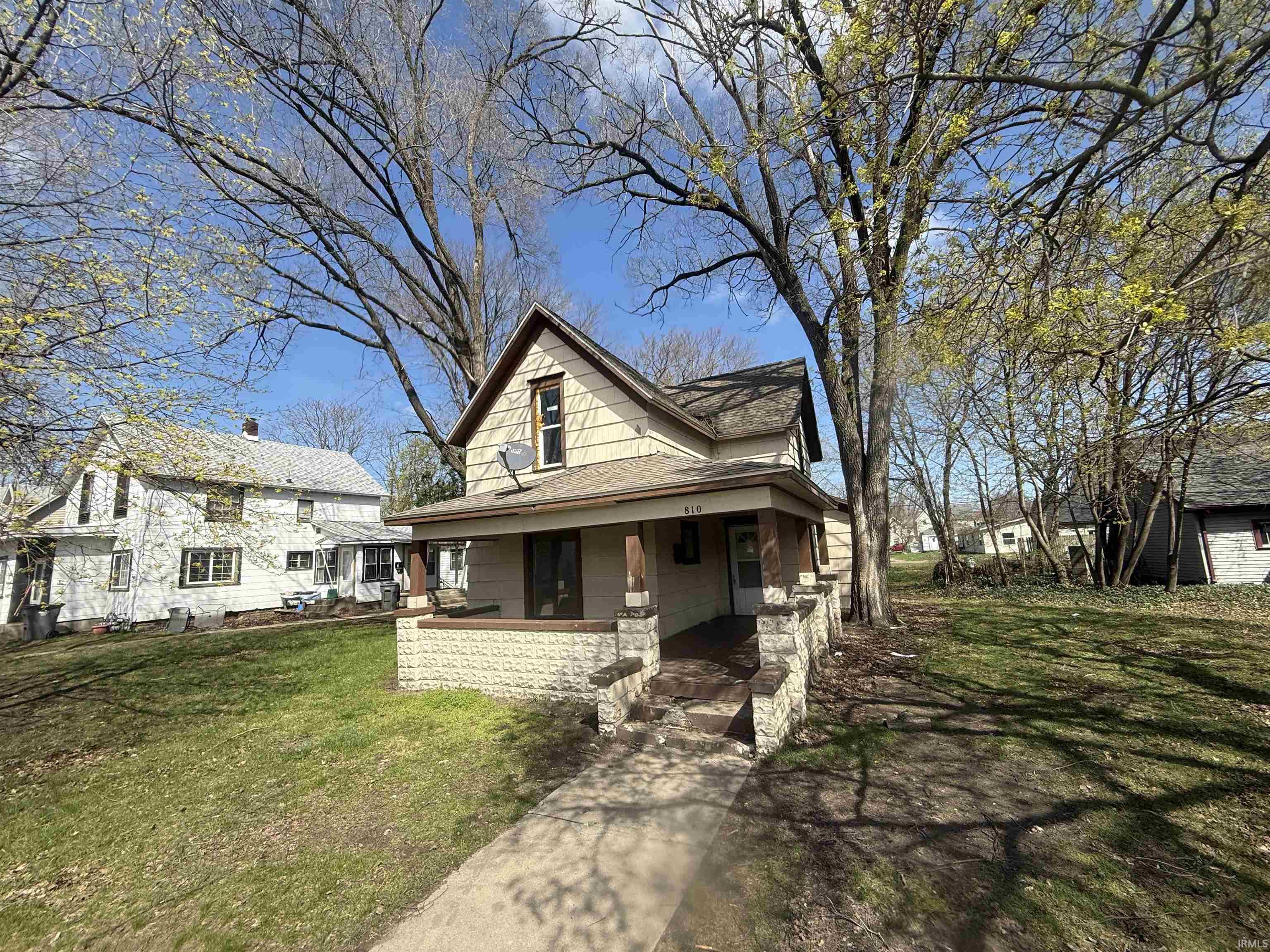 View of front facade with a porch, a front lawn, and roof with shingles