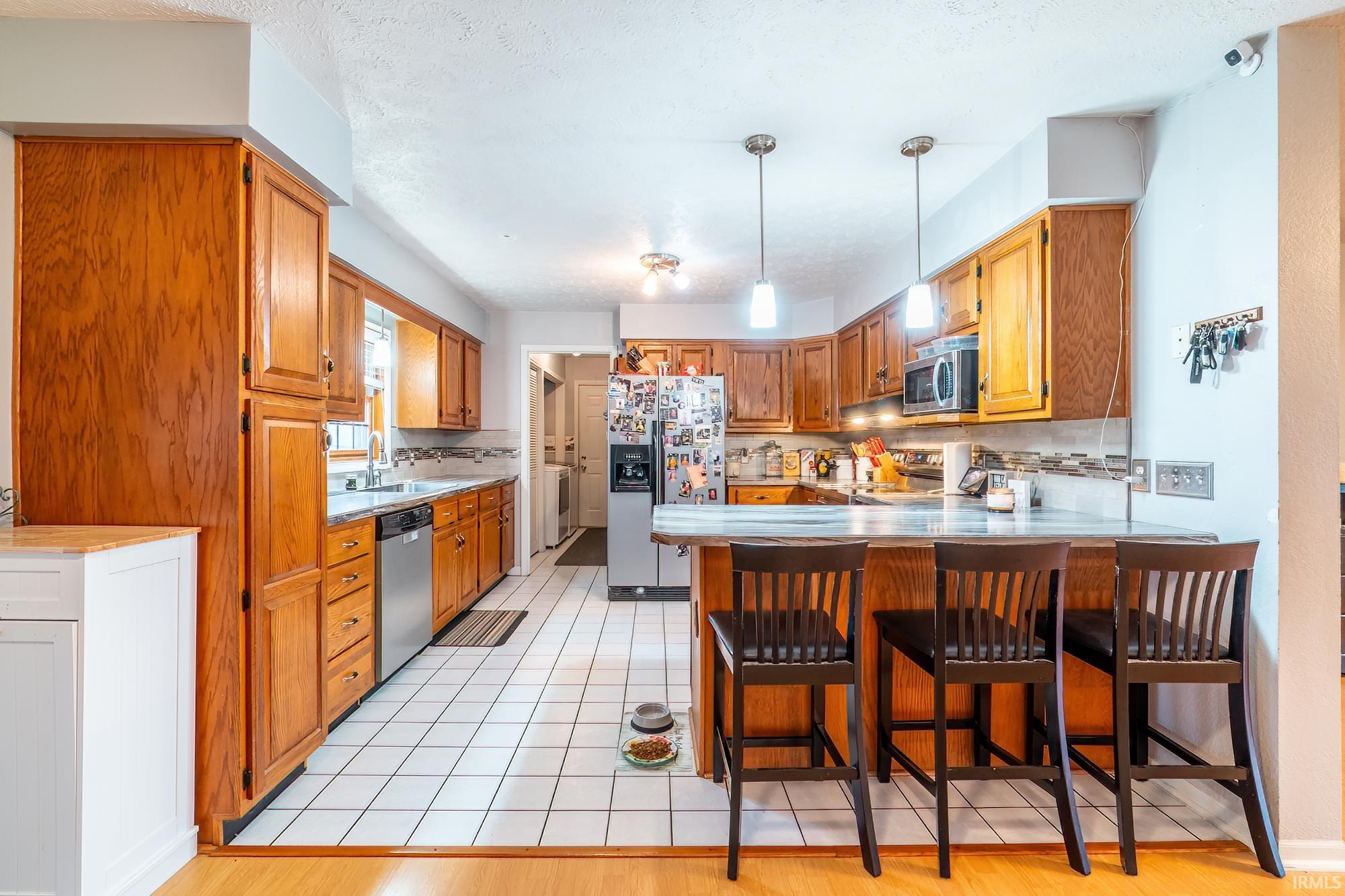 Kitchen with a peninsula, wood finish cabinets, stainless steel appliances, a breakfast bar, and light countertops